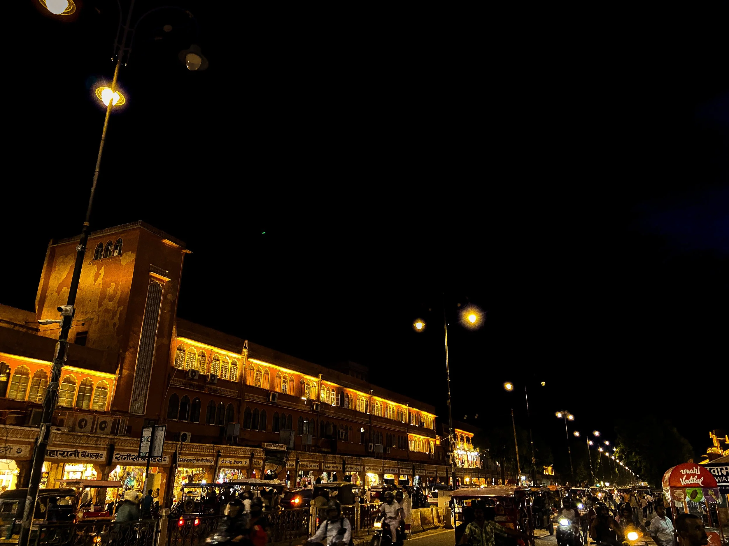 Nighttime street scene with large illuminated building and streetlights, busy with vehicles and people.