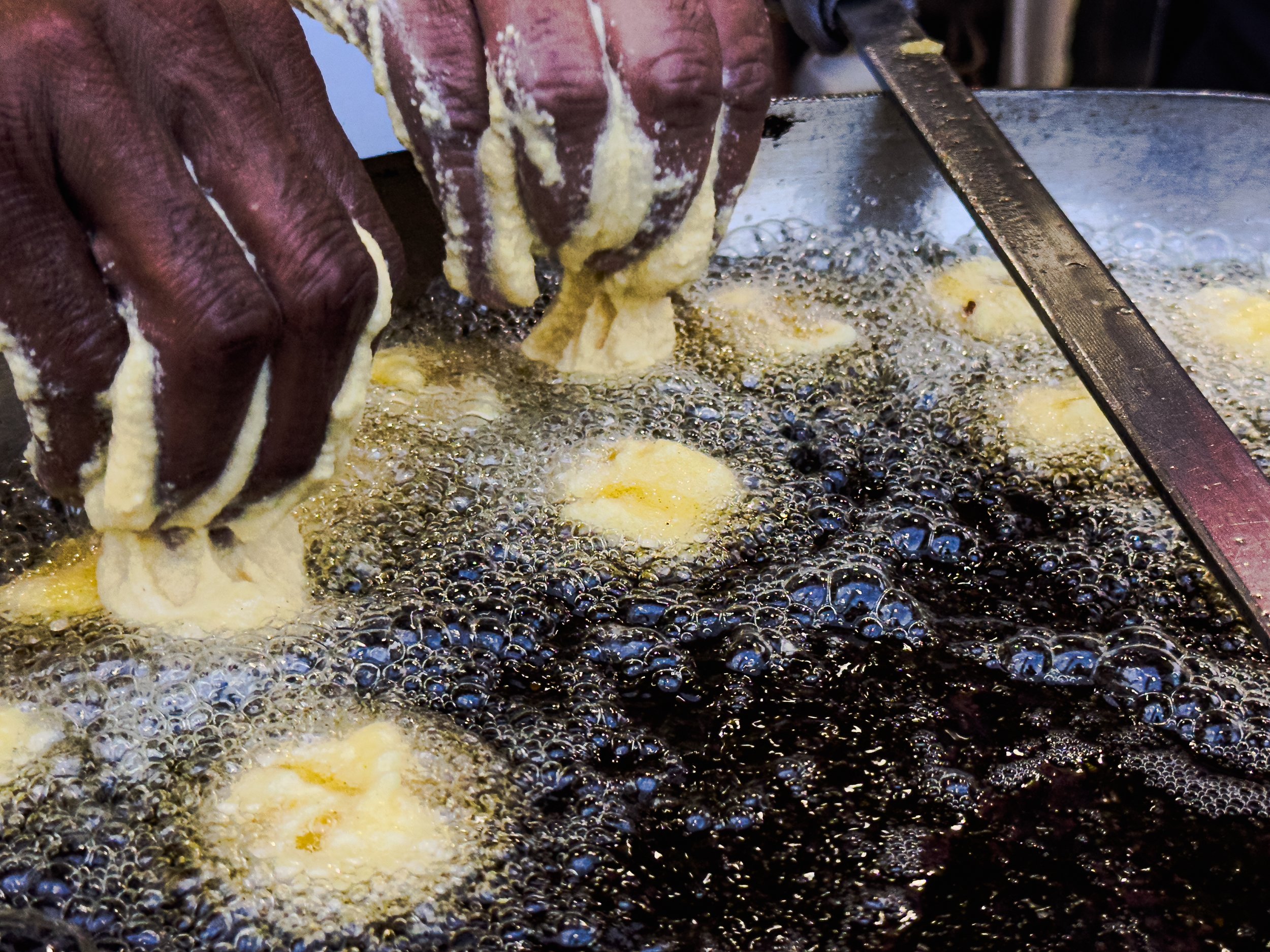 Hands frying dough in hot oil in a large pan.