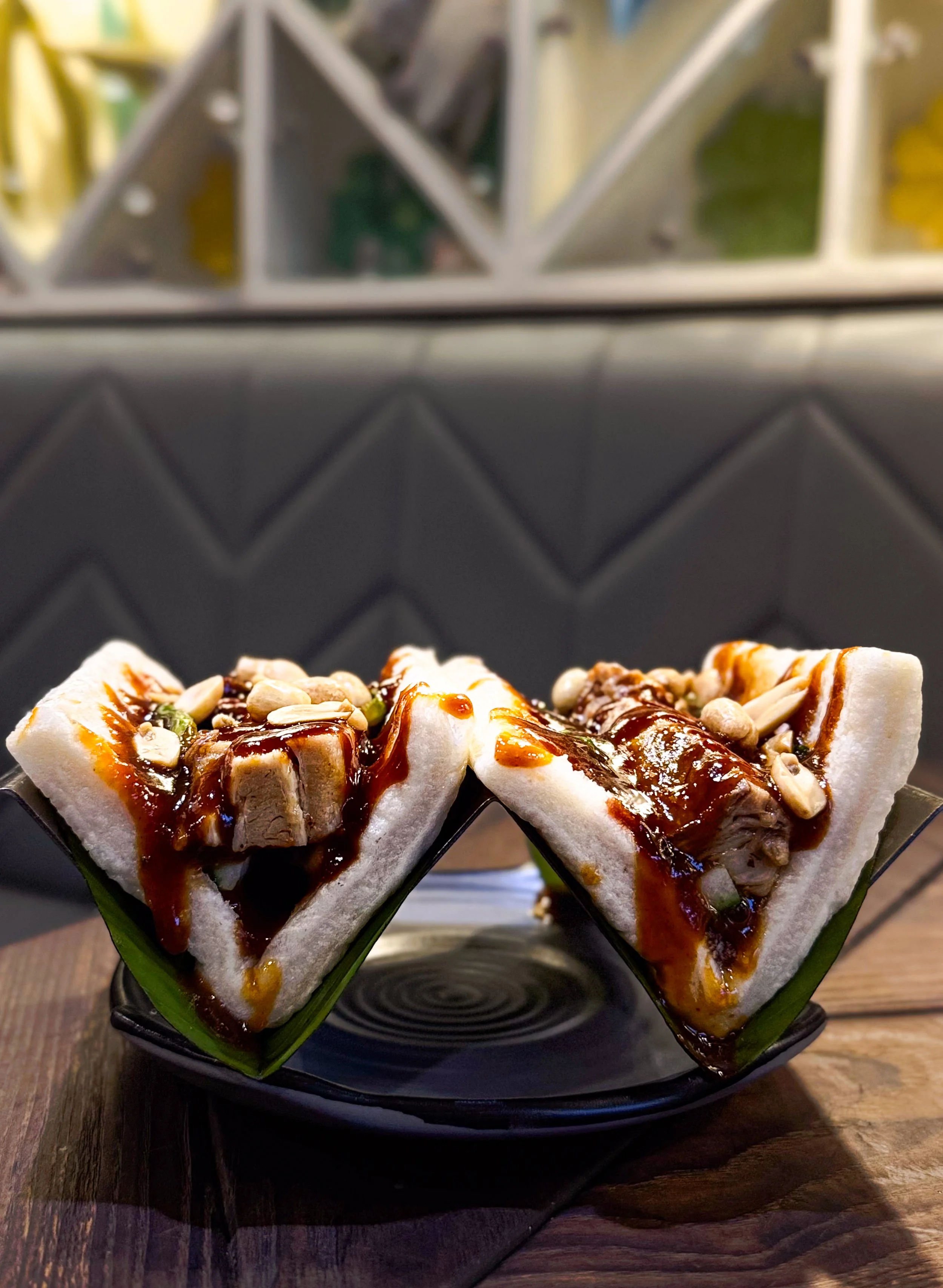 Two slices of banh mi sandwiches with pork, peanuts, and sauce on a black plate.