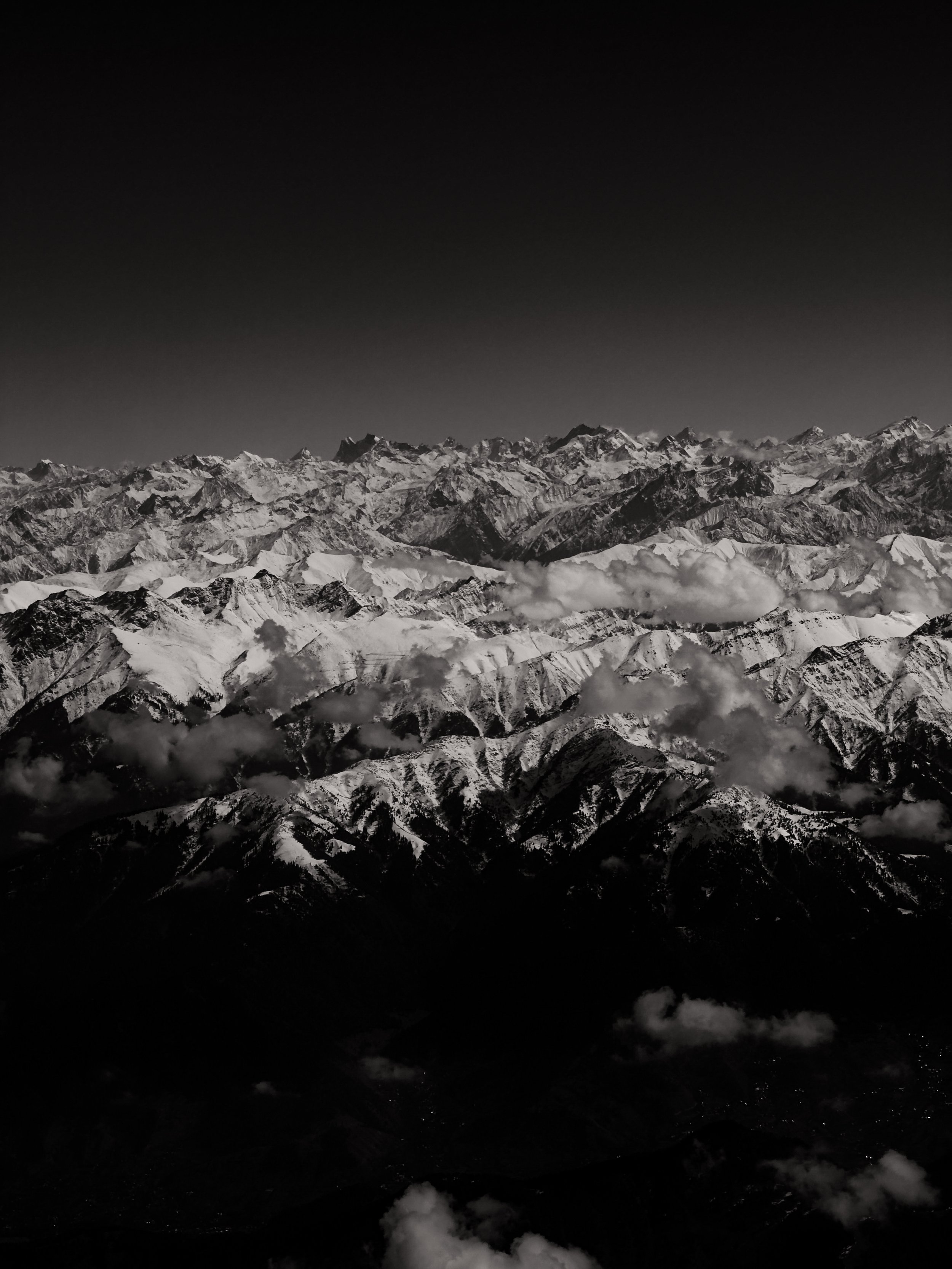 Black and white photo of snow-covered mountain range with clouds.
