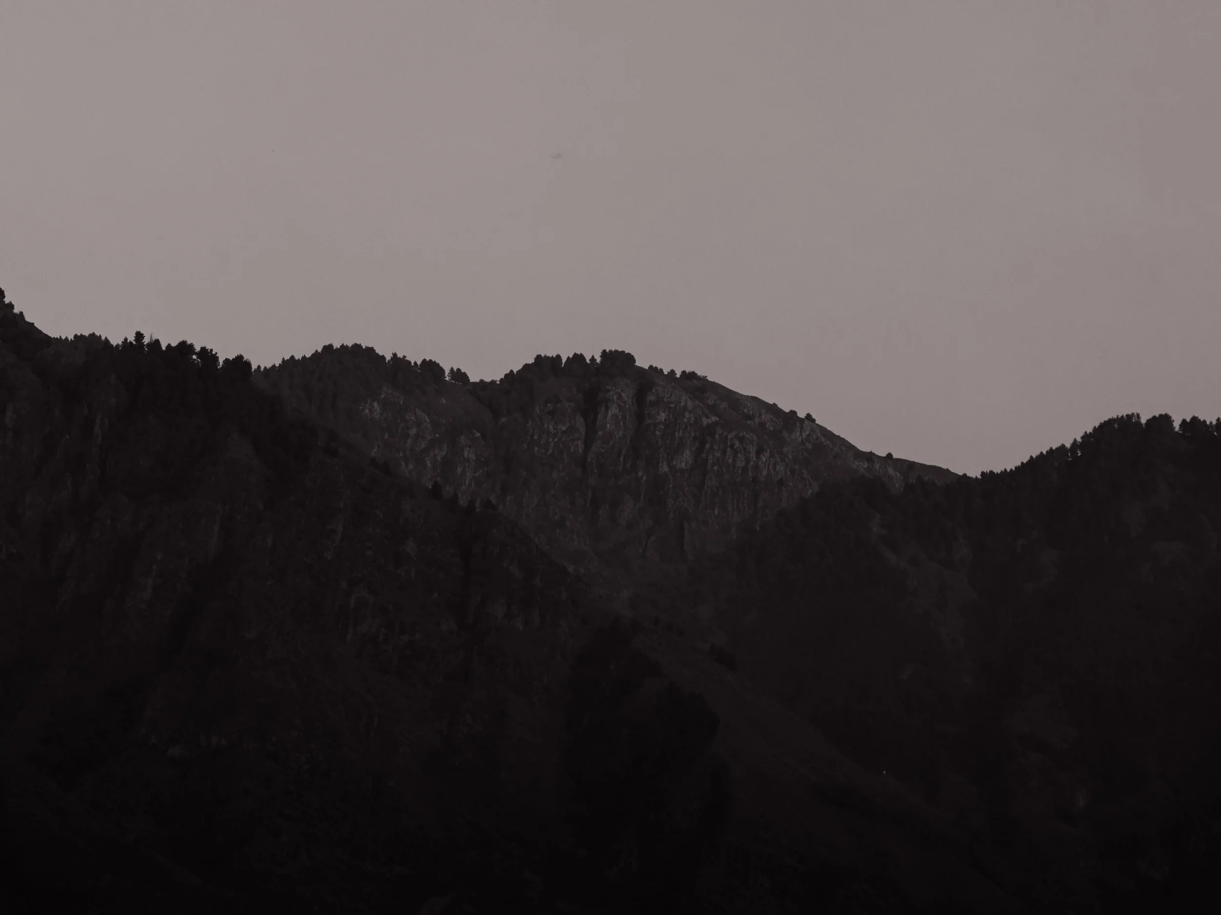 Dark silhouette of mountain range under a gray sky.