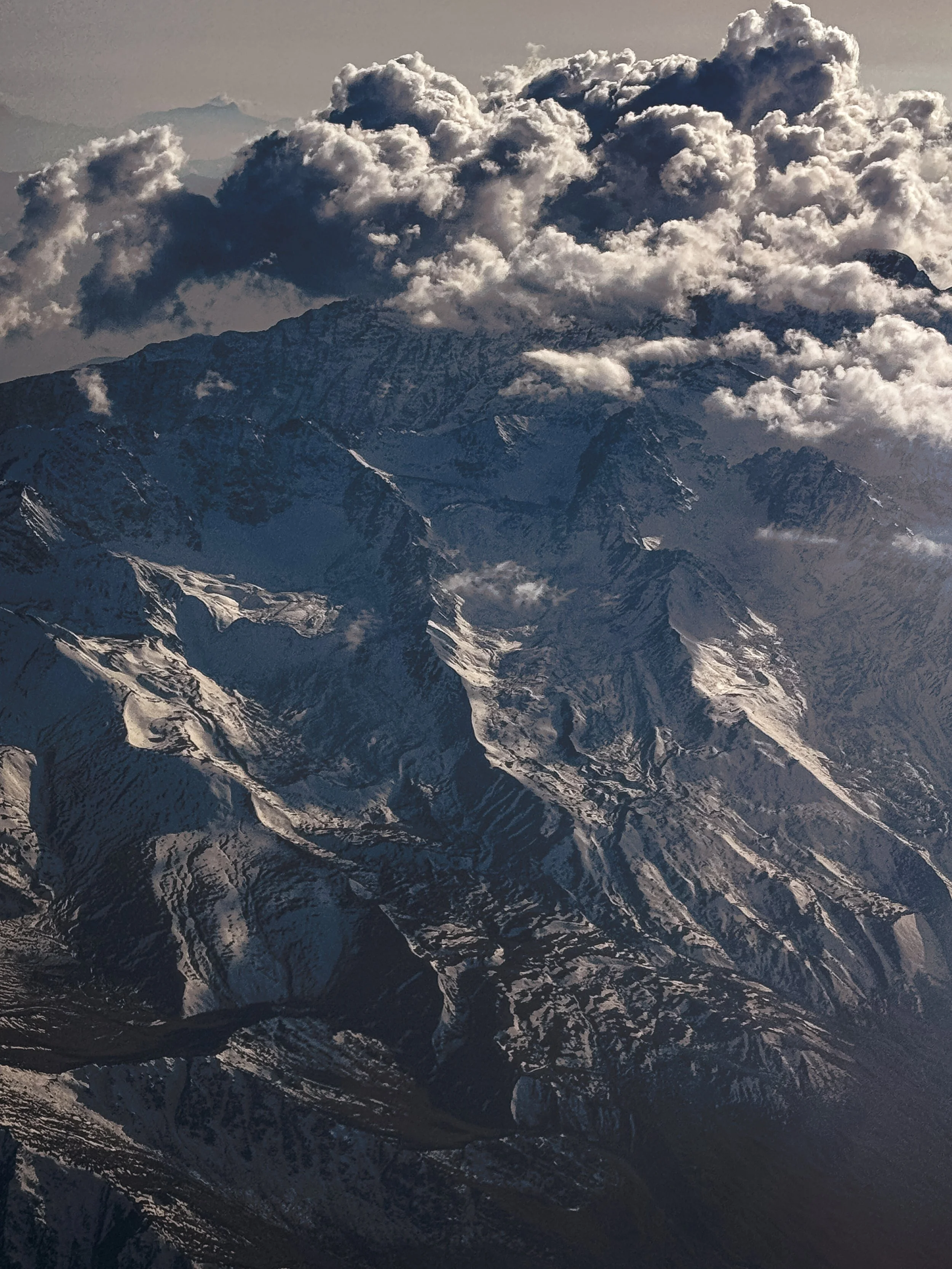 Snow-capped mountain range with rugged peaks and large cloud formation above.