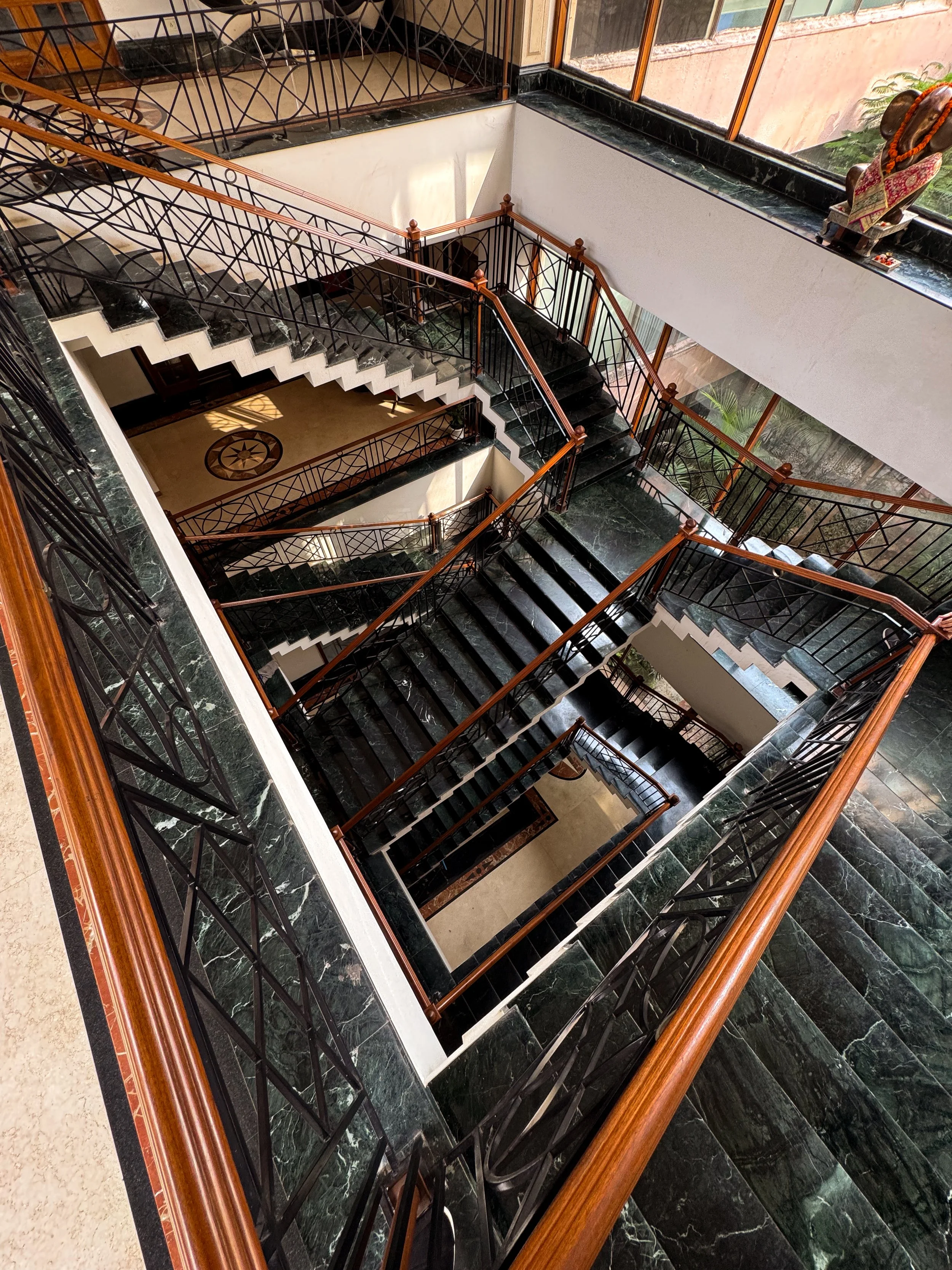 Multiple levels of staircases with black marble steps, wooden handrails, and decorative metal railings in a well-lit building interior.