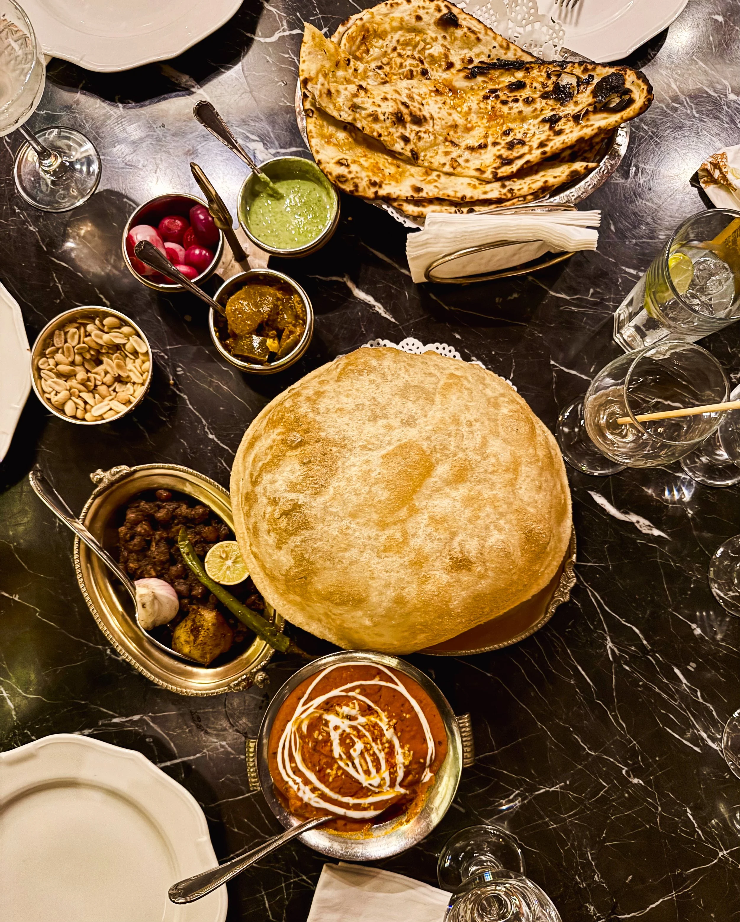 Indian meal with naan bread, curry, rice, and side dishes on a marble table.