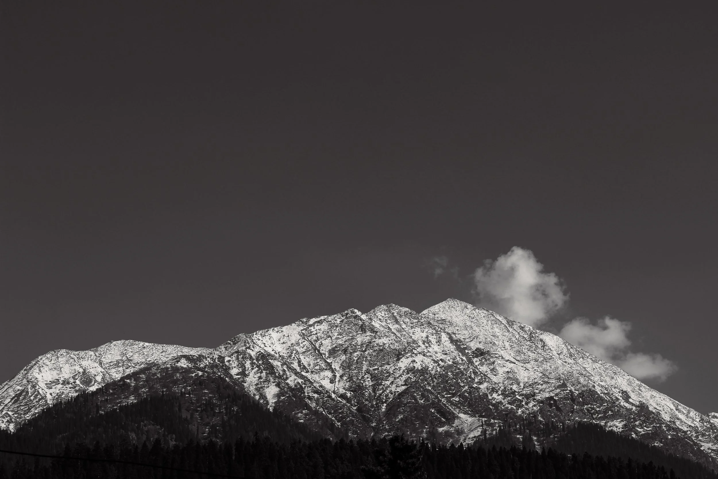 Snow-capped mountain peaks above a forest, with a few clouds in the sky.
