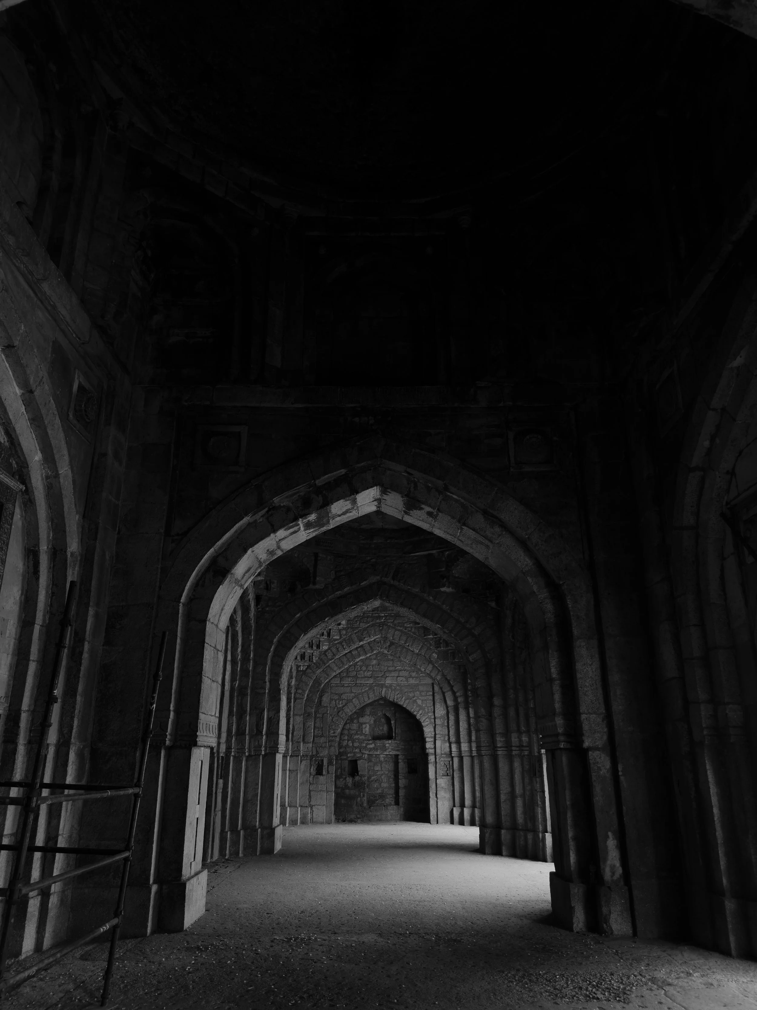 Arched stone corridor inside a historic building, dimly lit, black and white photo.