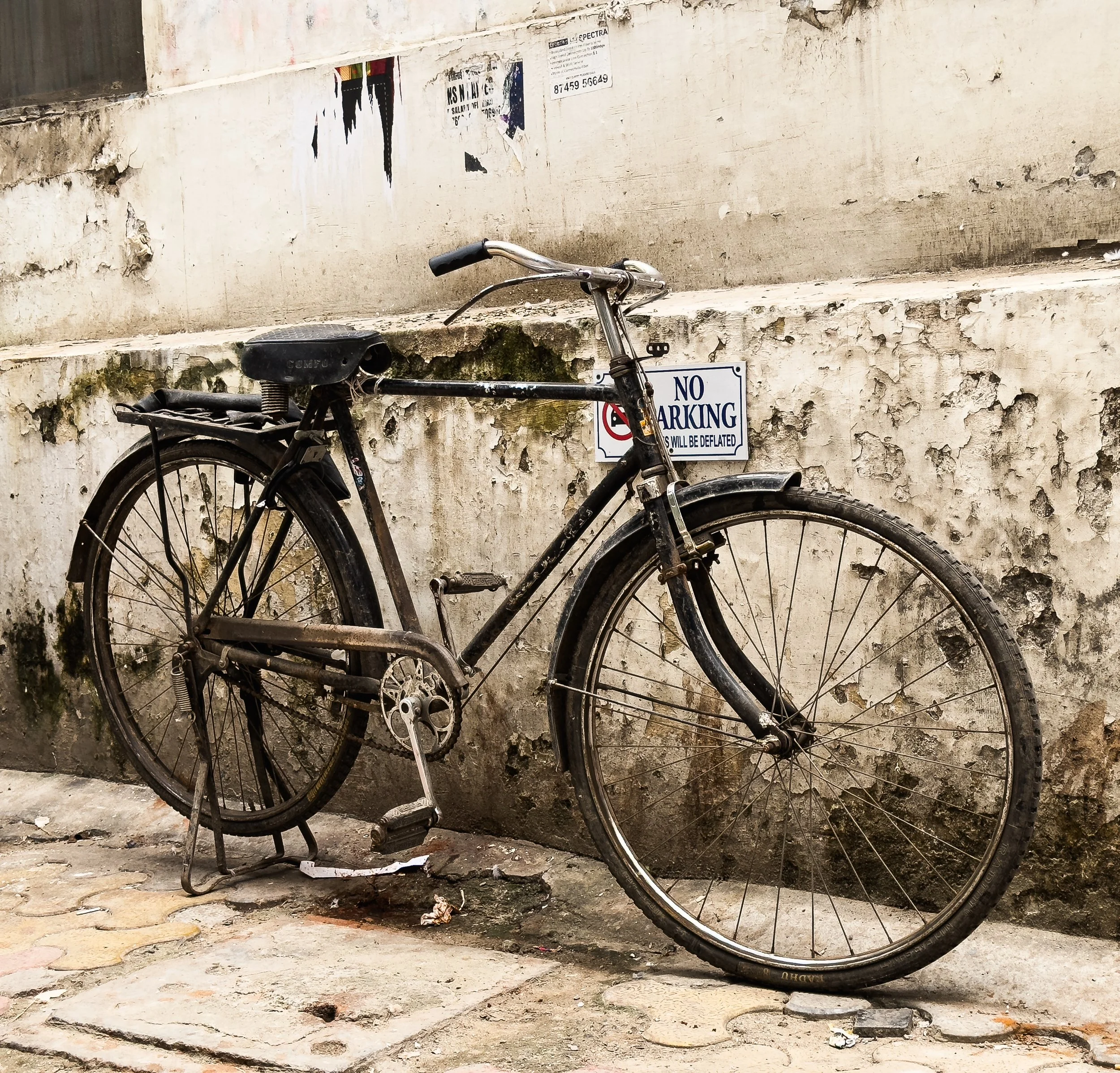 Old, rusty bicycle parked against a weathered concrete wall with a 'No Parking' sign.