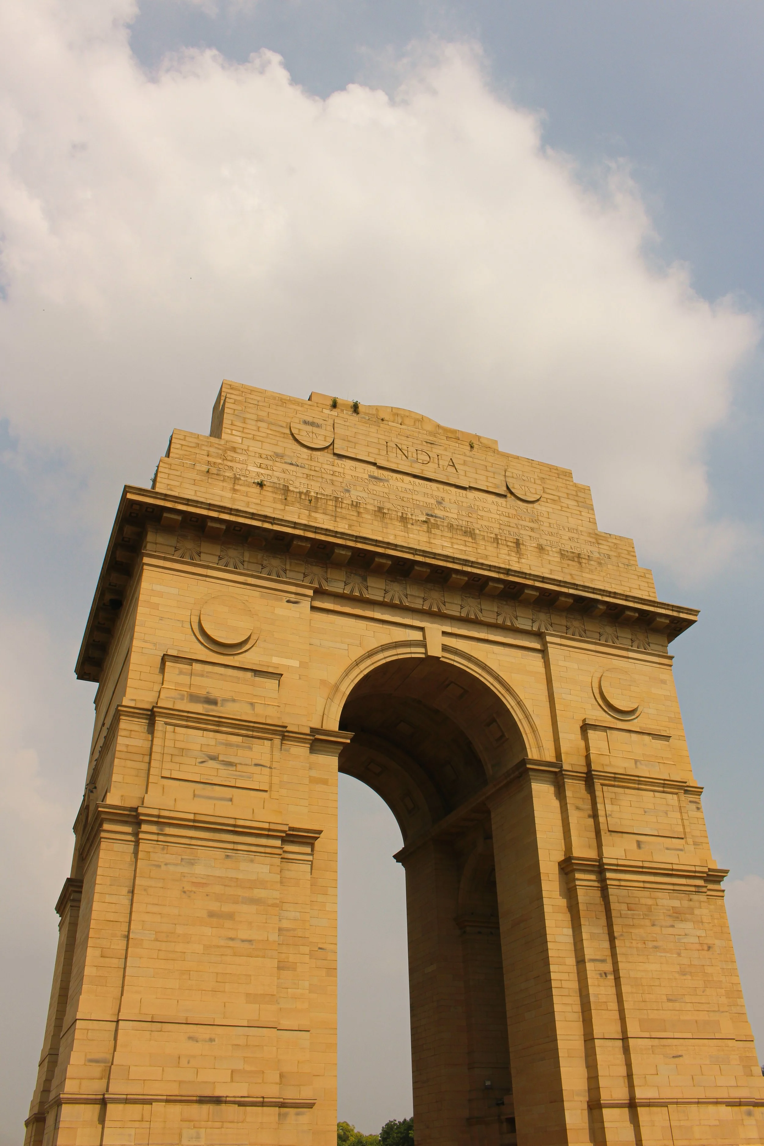 India Gate, a historic war memorial in Delhi, made of sandstone with an archway design, set against a cloudy sky.
