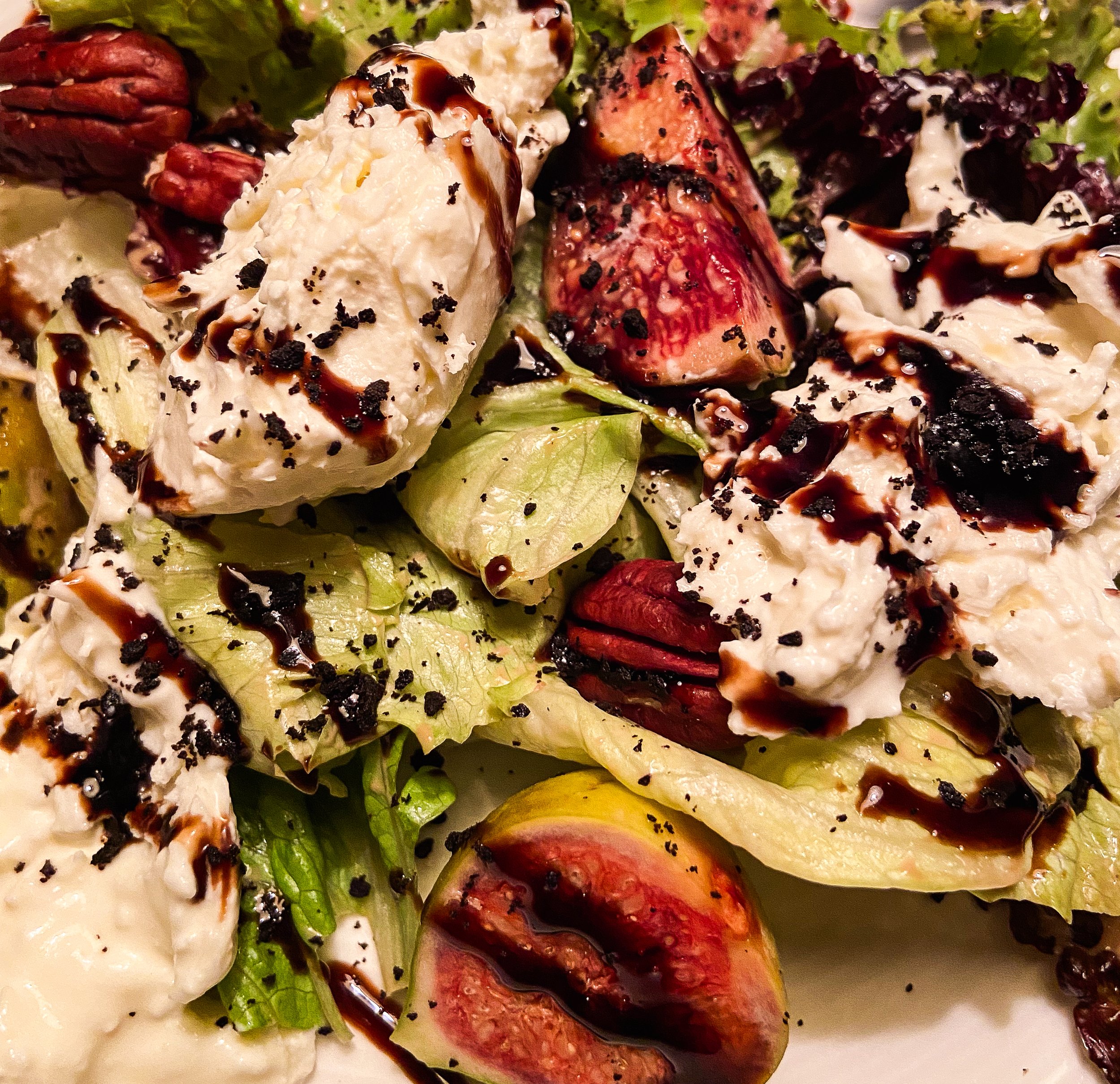 Close-up of a salad with lettuce, strawberries, cherry tomatoes, mozzarella cheese, pecans, balsamic glaze, and black pepper.