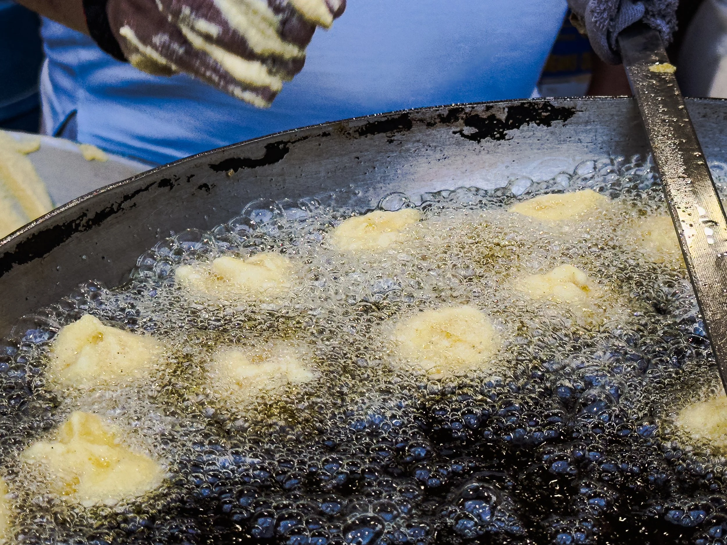 Frying small pieces of dough in hot oil in a deep pan.