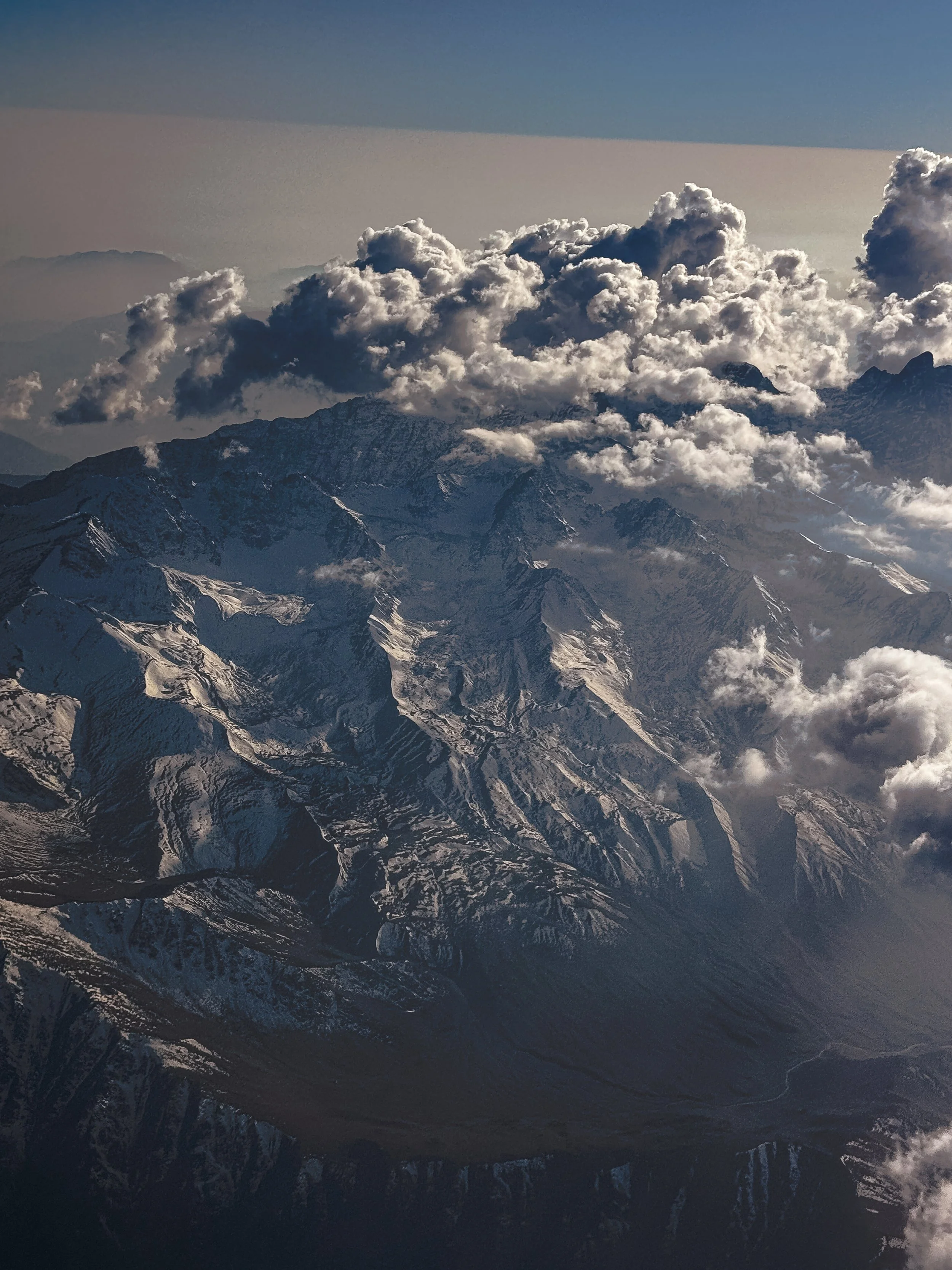 Snow-capped mountain peaks with clouds in a clear sky.