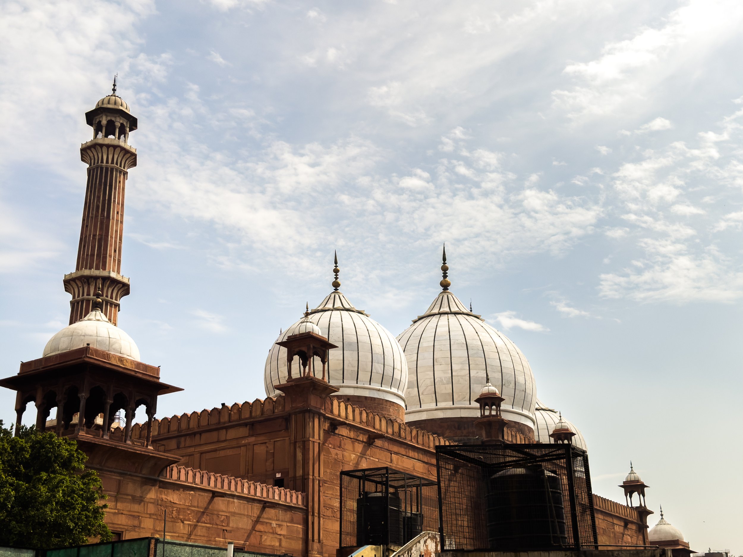 A historic mosque with white domes and a tall minaret, set against a partly cloudy sky.