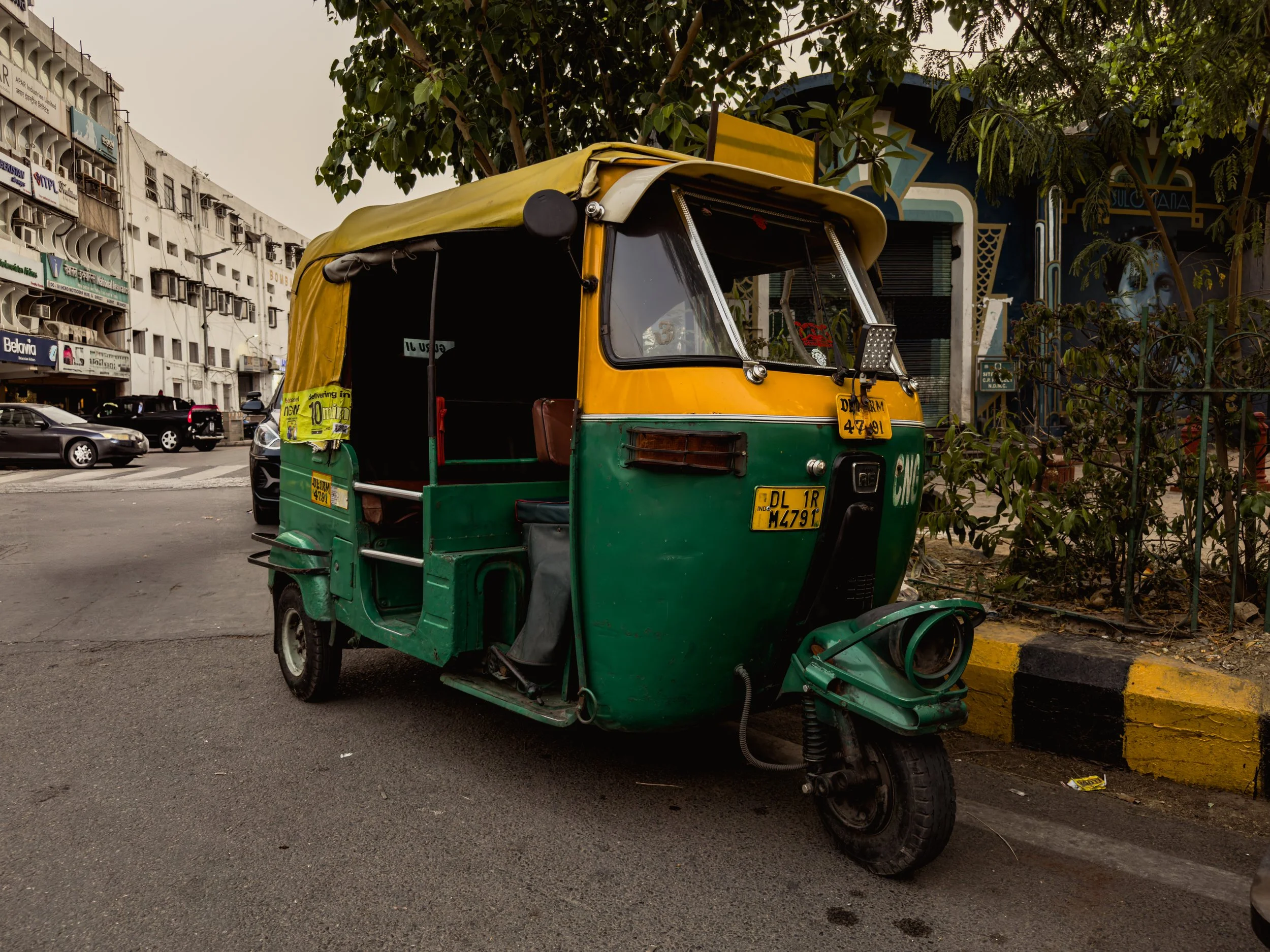 Colorful auto rickshaw parked on city street with urban buildings and trees in background.