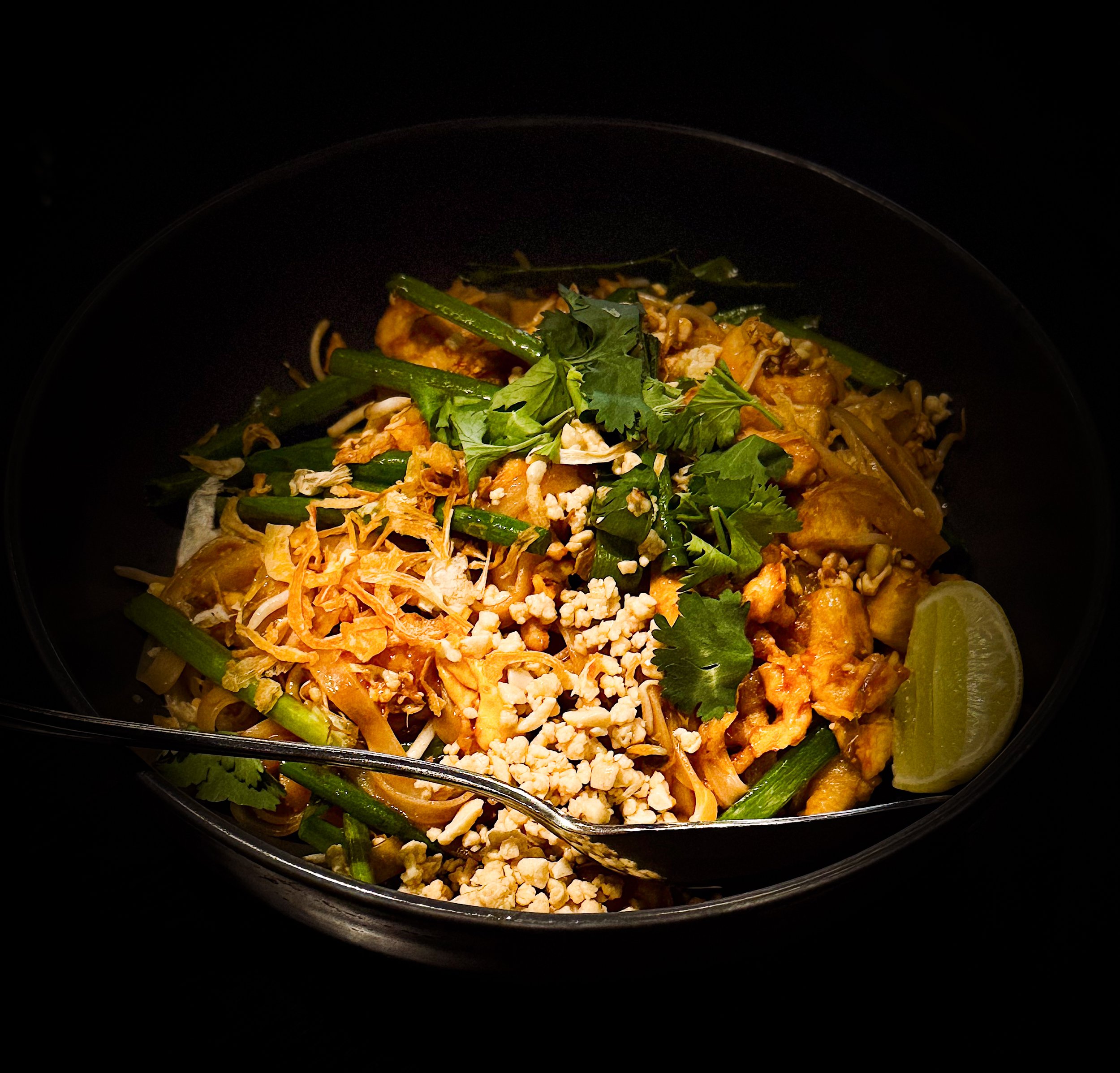 Bowl of pad thai with chopped peanuts, cilantro, lime wedge, and stir-fried vegetables.