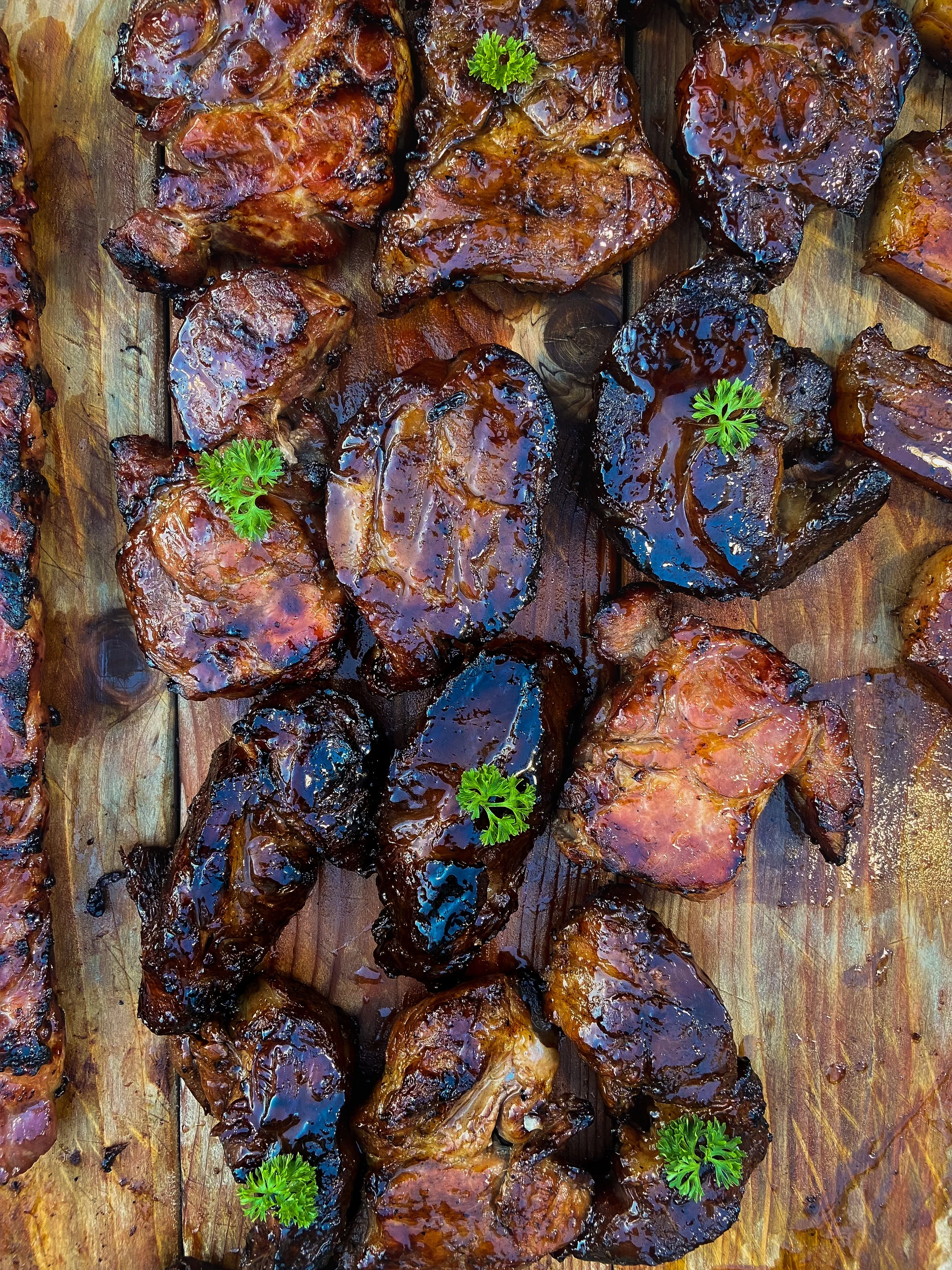 Barbecue pork ribs with a glossy dark barbecue sauce, garnished with sprigs of parsley on a wooden cutting board.