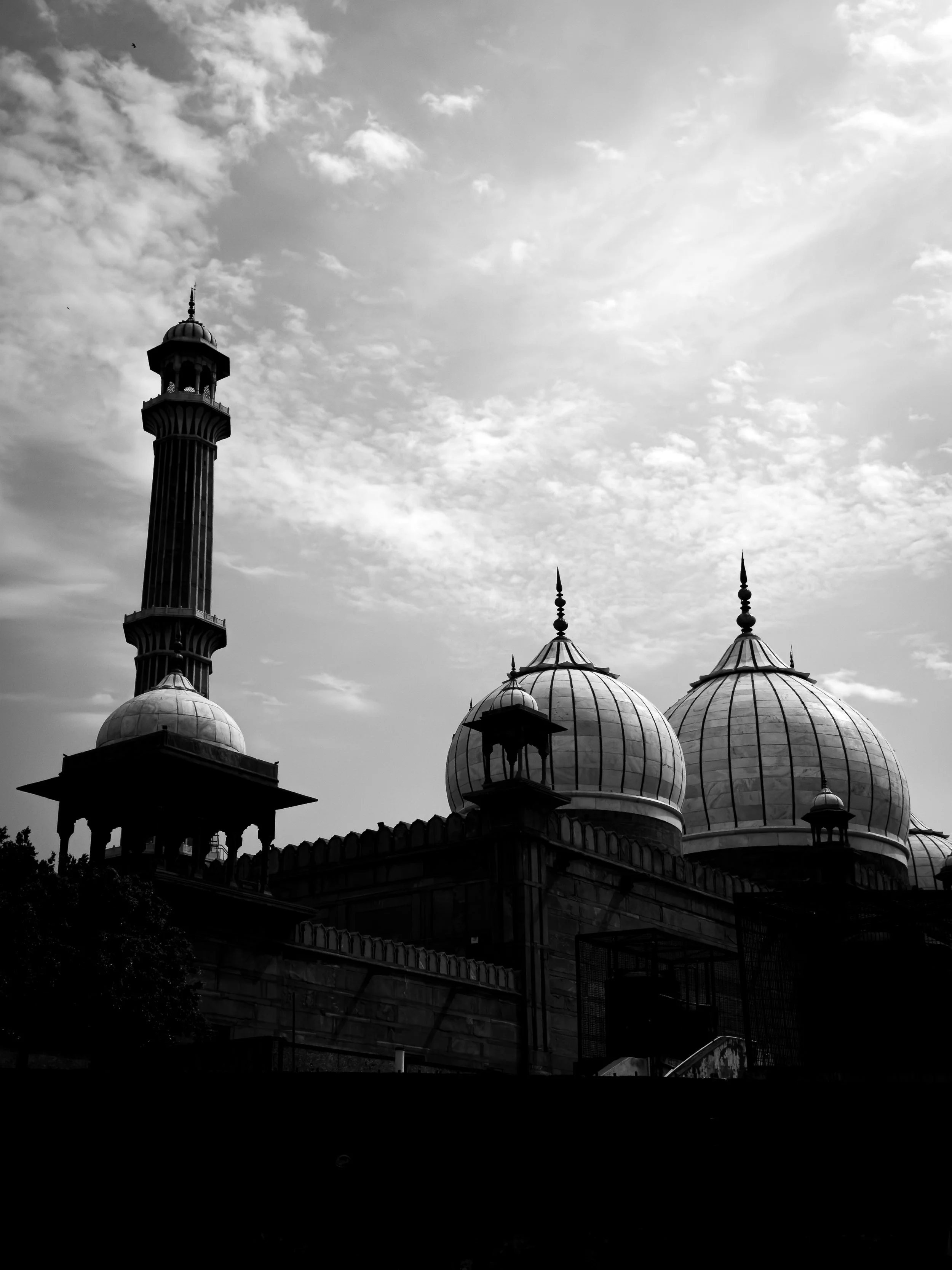 Black and white photo of a mosque with domes and a tall minaret, with a cloudy sky in the background.