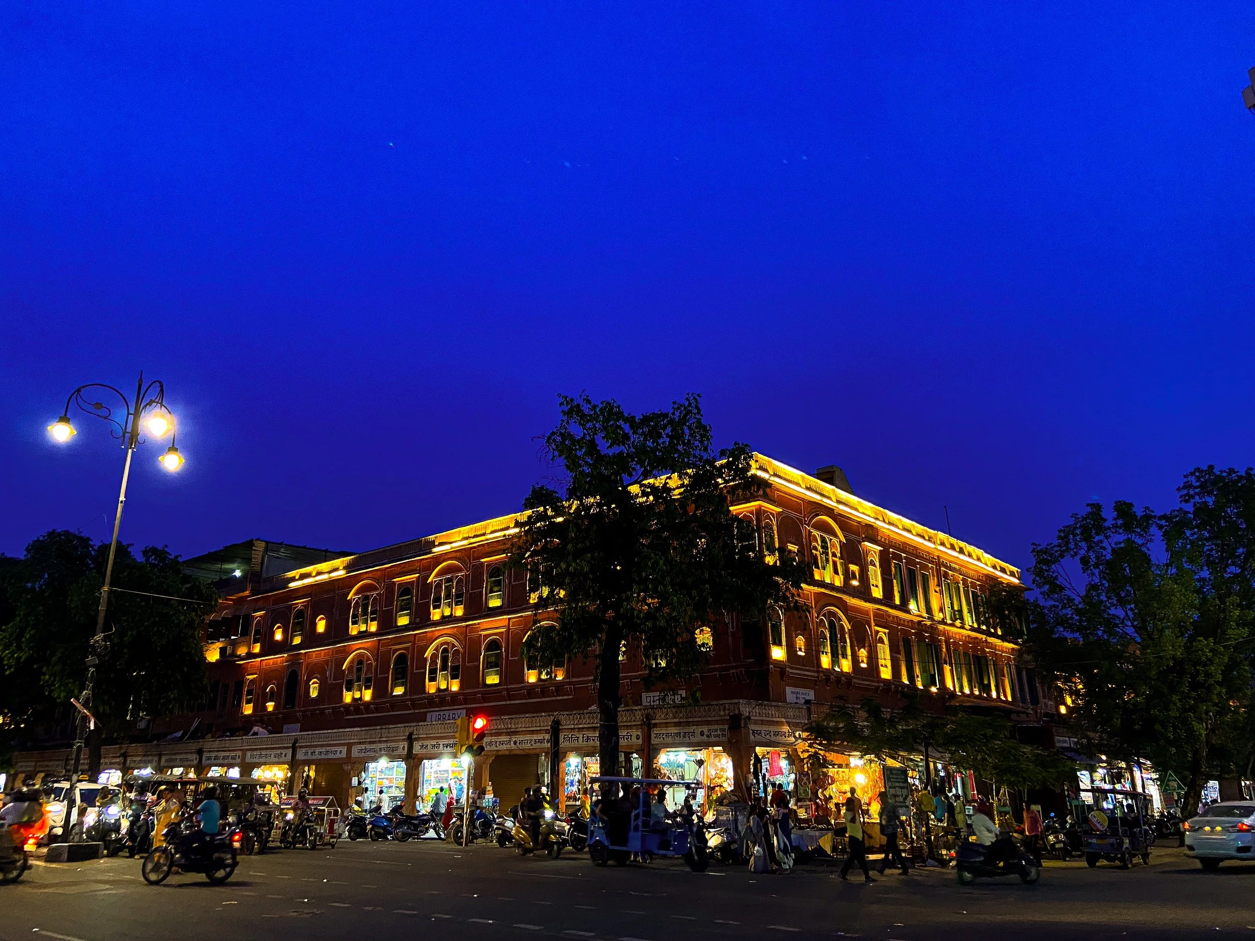 Night view of a busy street with an illuminated multi-story building, streetlights, and numerous vehicles and pedestrians.