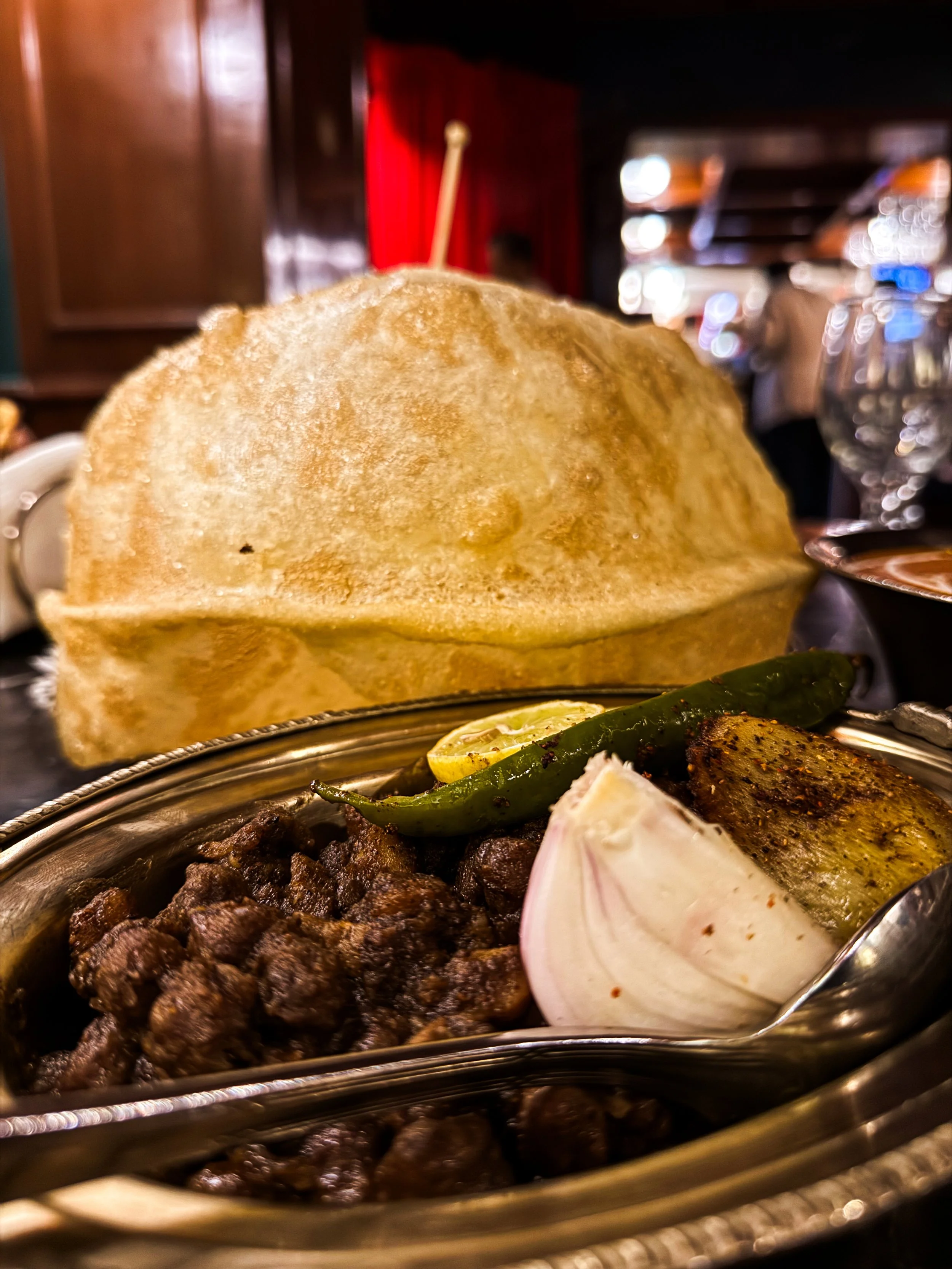 Indian meal with naan bread, grilled meat, grilled green chilies, lemon, and sliced onion served in a metal dish.