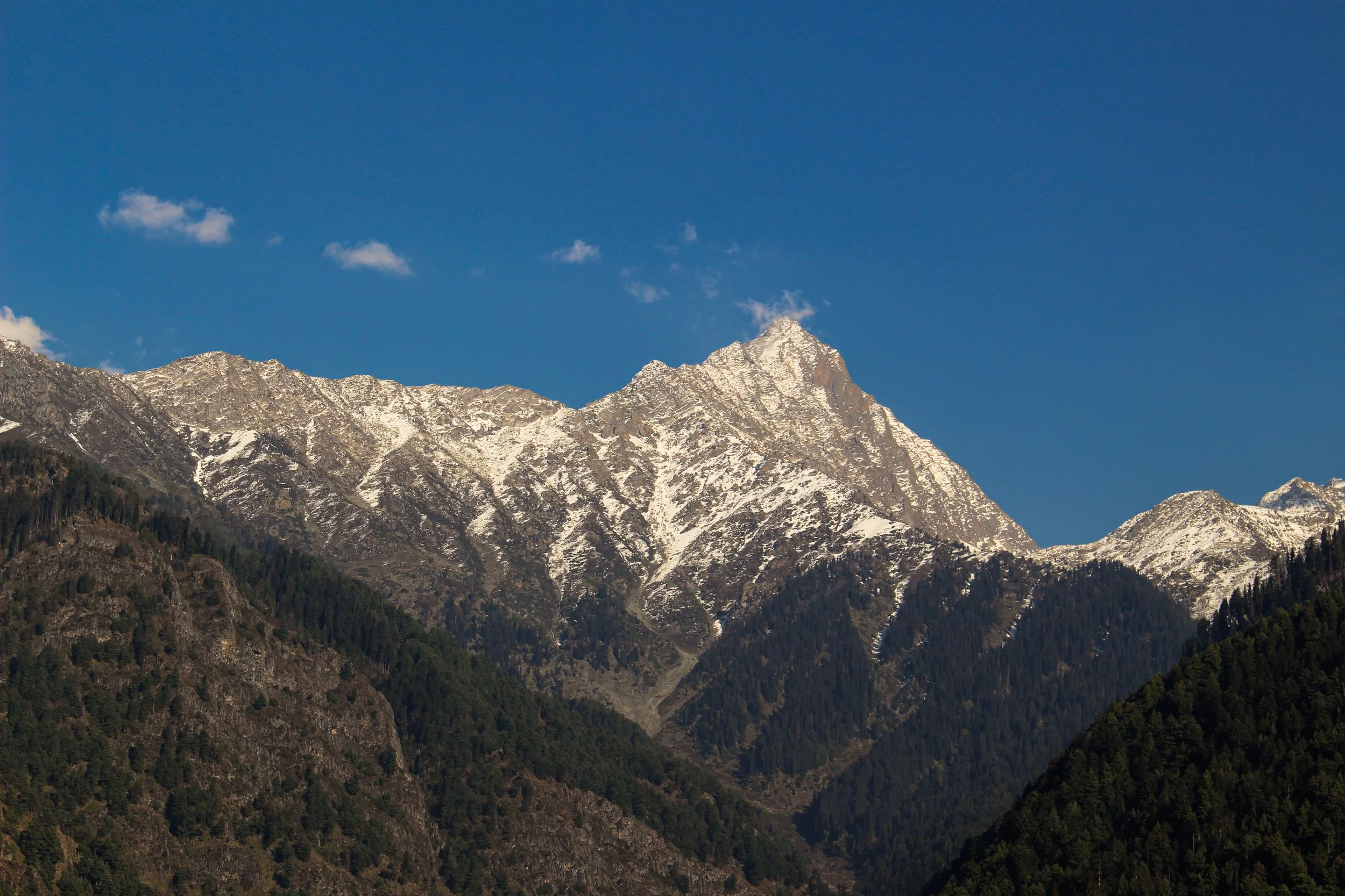 A mountain with snow-capped peaks against a clear blue sky with a few small clouds.