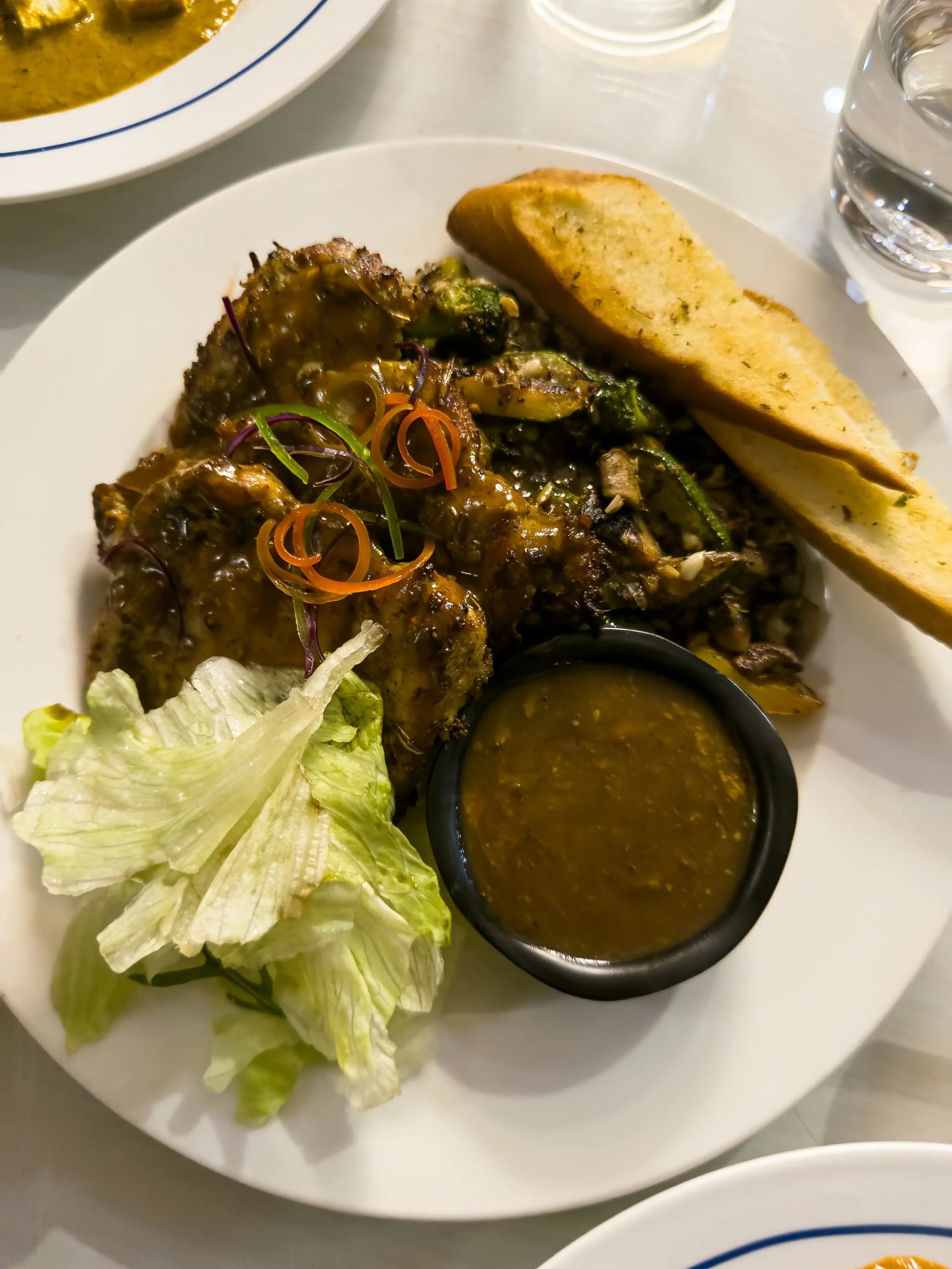Plate of chicken wings with sauce, a side of lettuce, two slices of garlic bread, a small bowl of dipping sauce, and a glass of water.