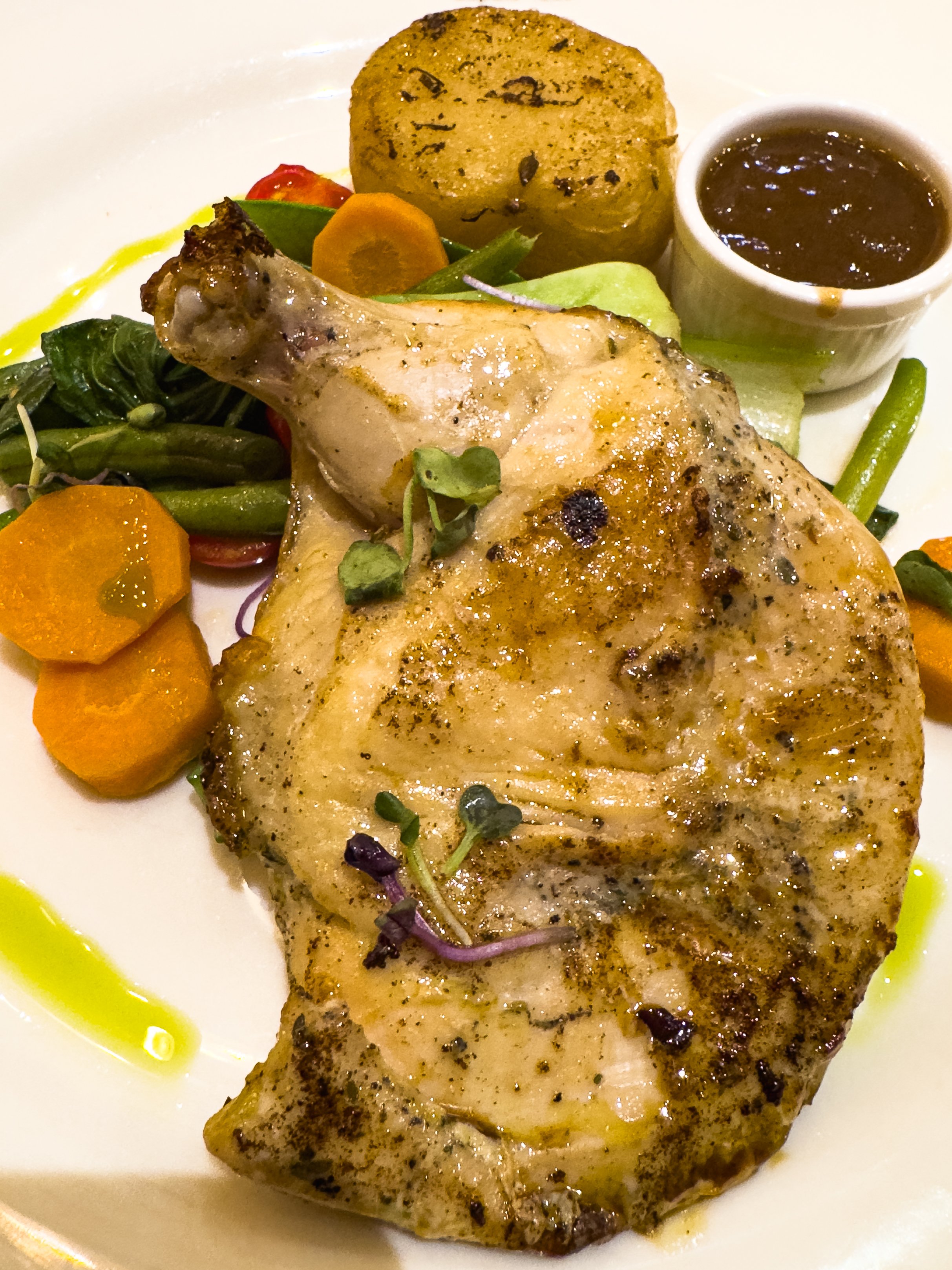 Grilled chicken thigh with herbs served with mixed vegetables, a baked potato, and dipping sauce.