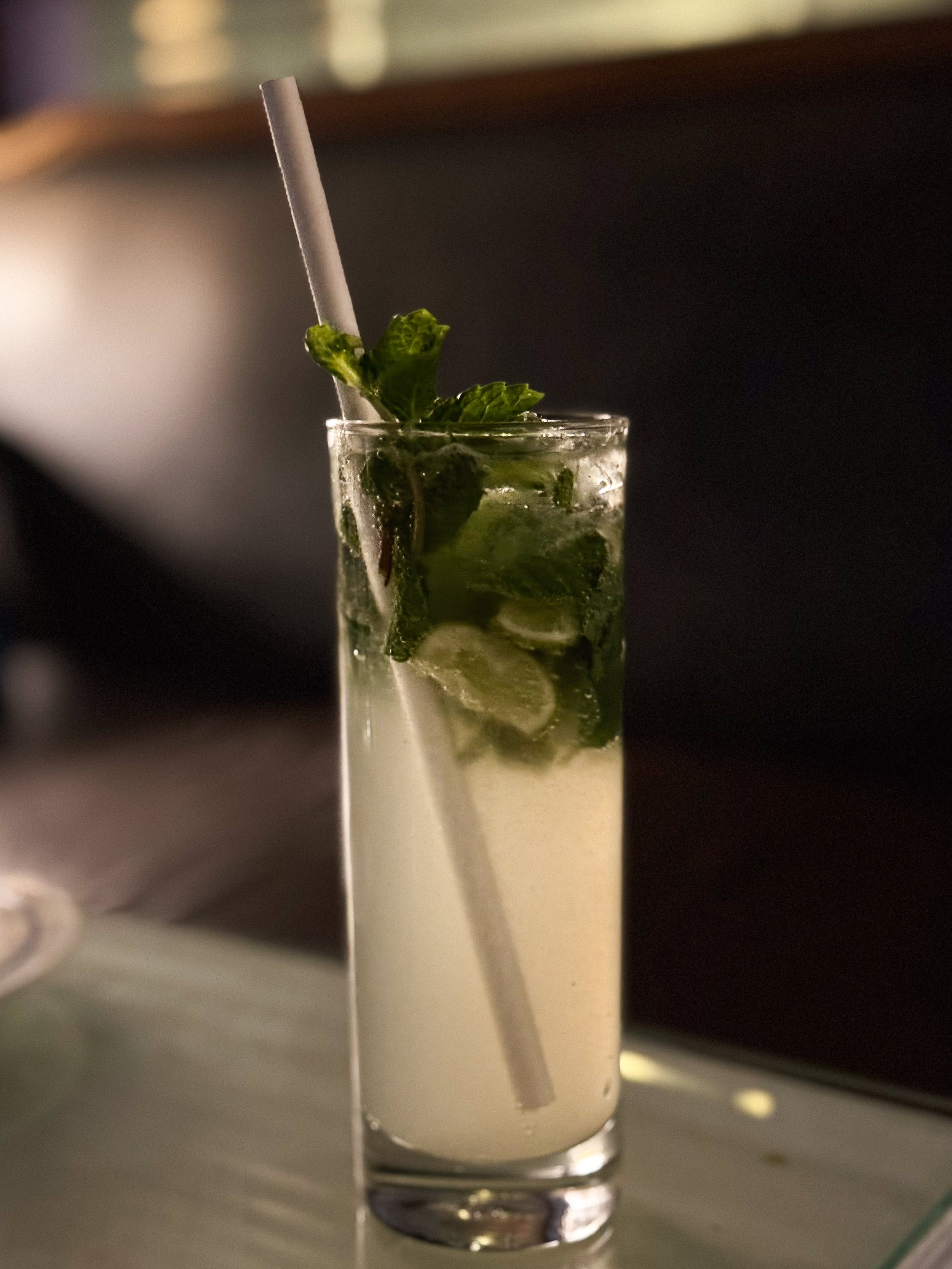 A tall glass of mojito cocktail with mint leaves, lime slices, ice cubes, a straw, and a sprig of mint garnish.