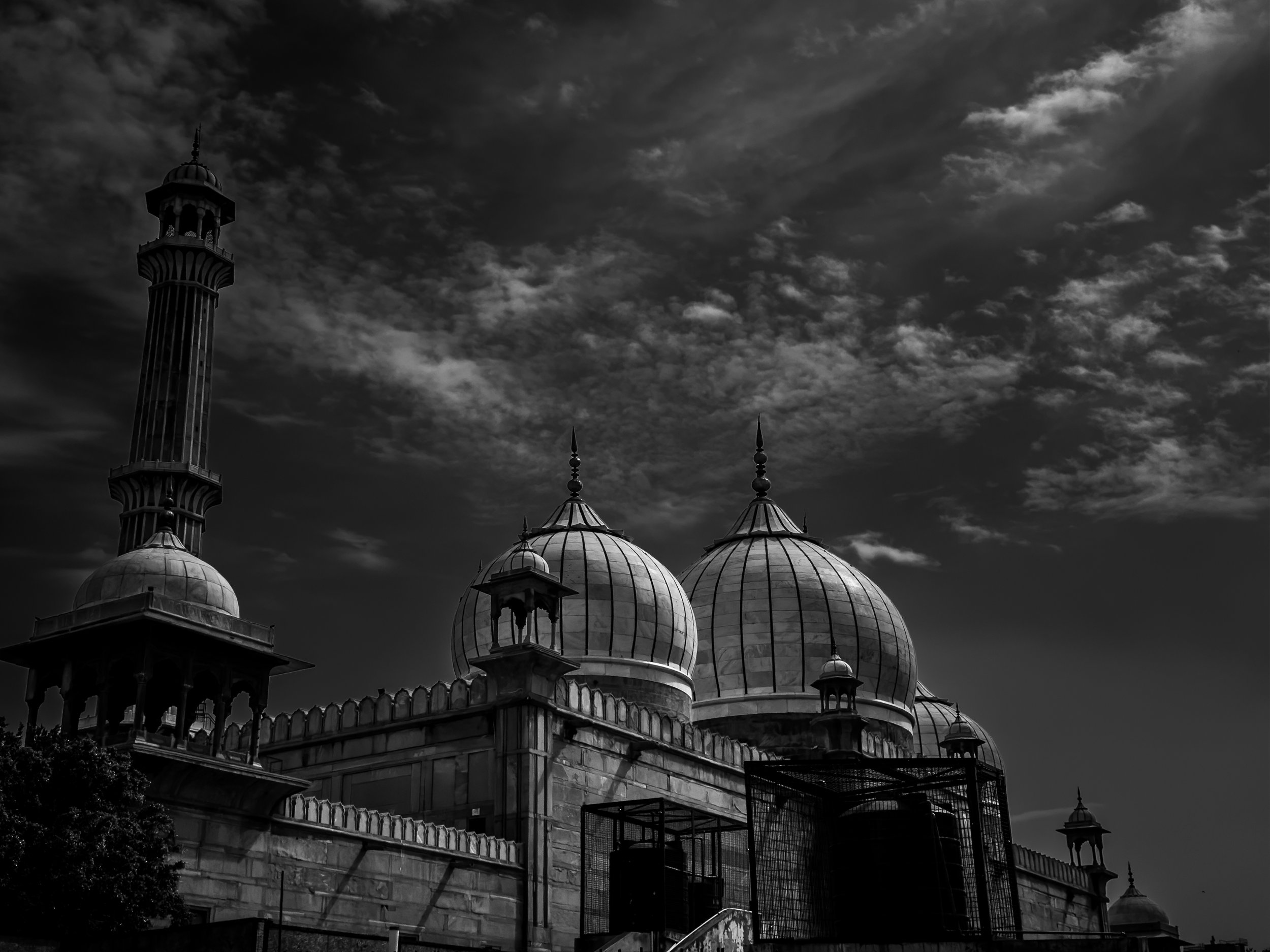A black and white photo of a mosque with multiple domes and minarets, set against a cloudy sky.