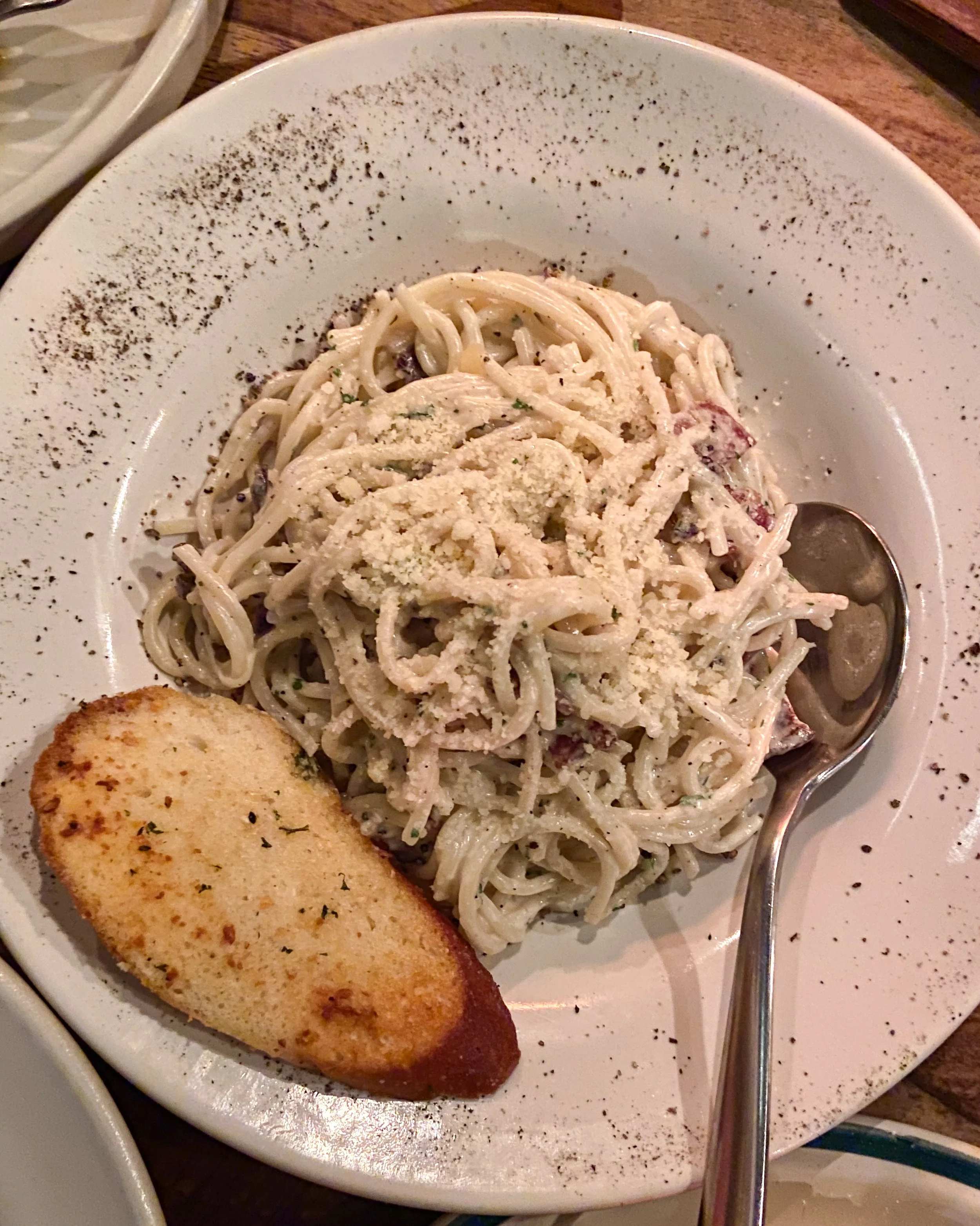 Plate of creamy pasta topped with grated cheese, accompanied by a toasted bread slice and a spoon on the side.
