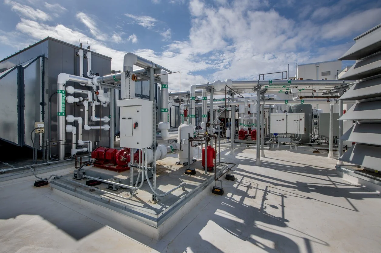 Chemical plant utility area featuring industrial air compression packages and process piping manifolds.
