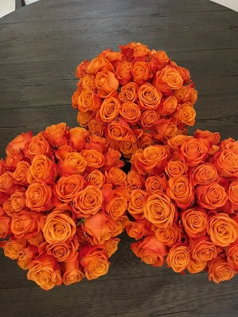 Three large bouquets of orange roses on a dark wooden surface.