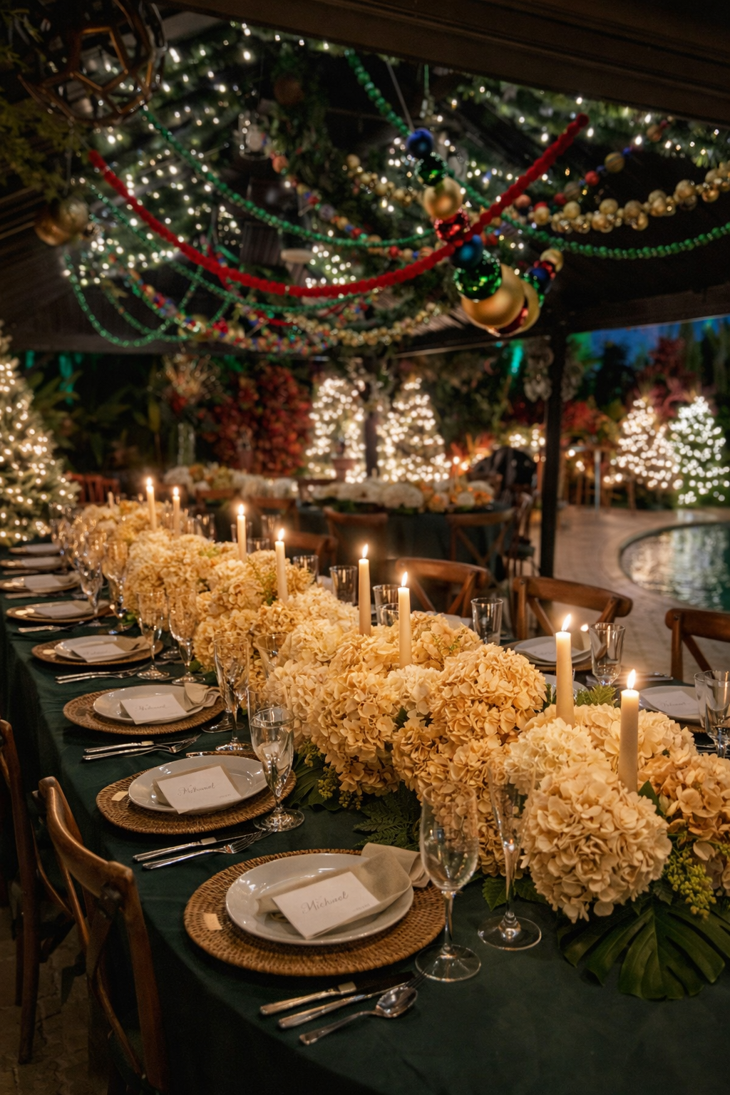 A long dining table decorated with cream-colored hydrangea floral arrangements and tall white candles. The table is set with white plates, silverware, wine glasses, and place cards. The background features decorated Christmas trees, string lights, an