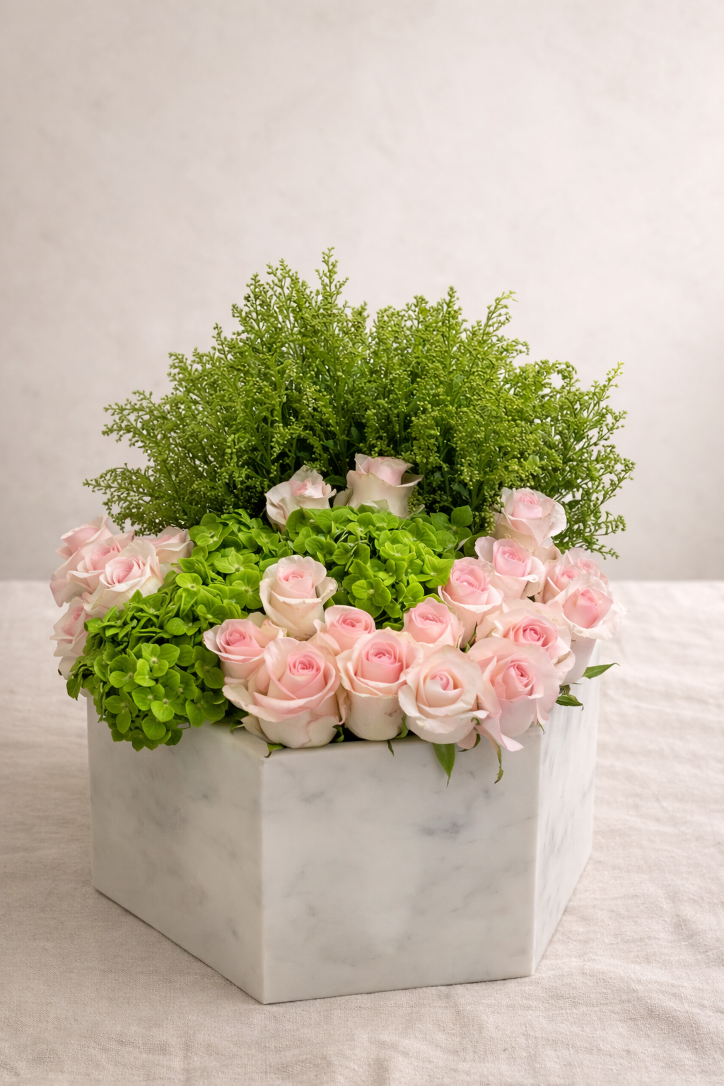 A white marble hexagonal flower box filled with pink roses, green hydrangeas, and green foliage against a neutral background.