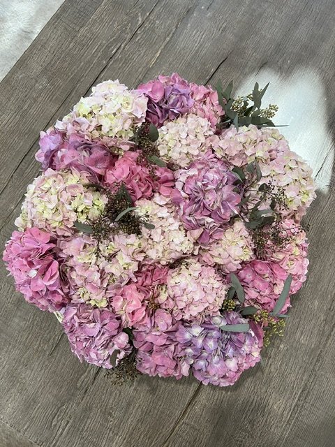 A bouquet of pink and white hydrangea flowers with some greenery, arranged on a wooden surface.