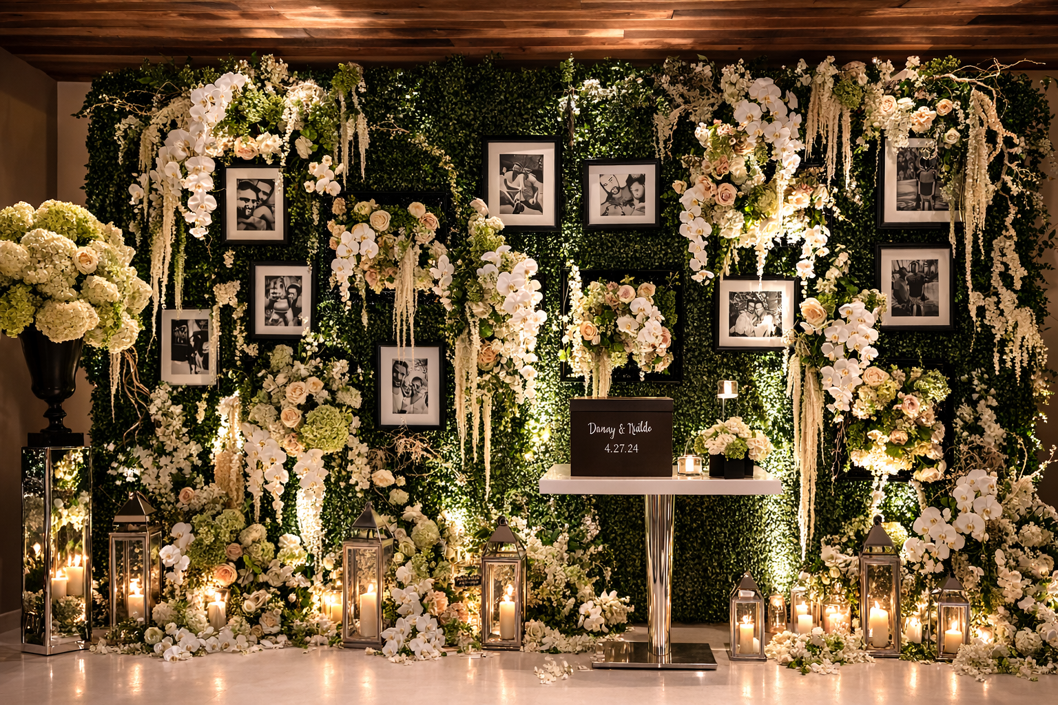 Elegant wedding backdrop decorated with white and blush flowers, candles, and black photo frames, with a table displaying the names 'Danny & Valdo' and date '4.27.24'.
