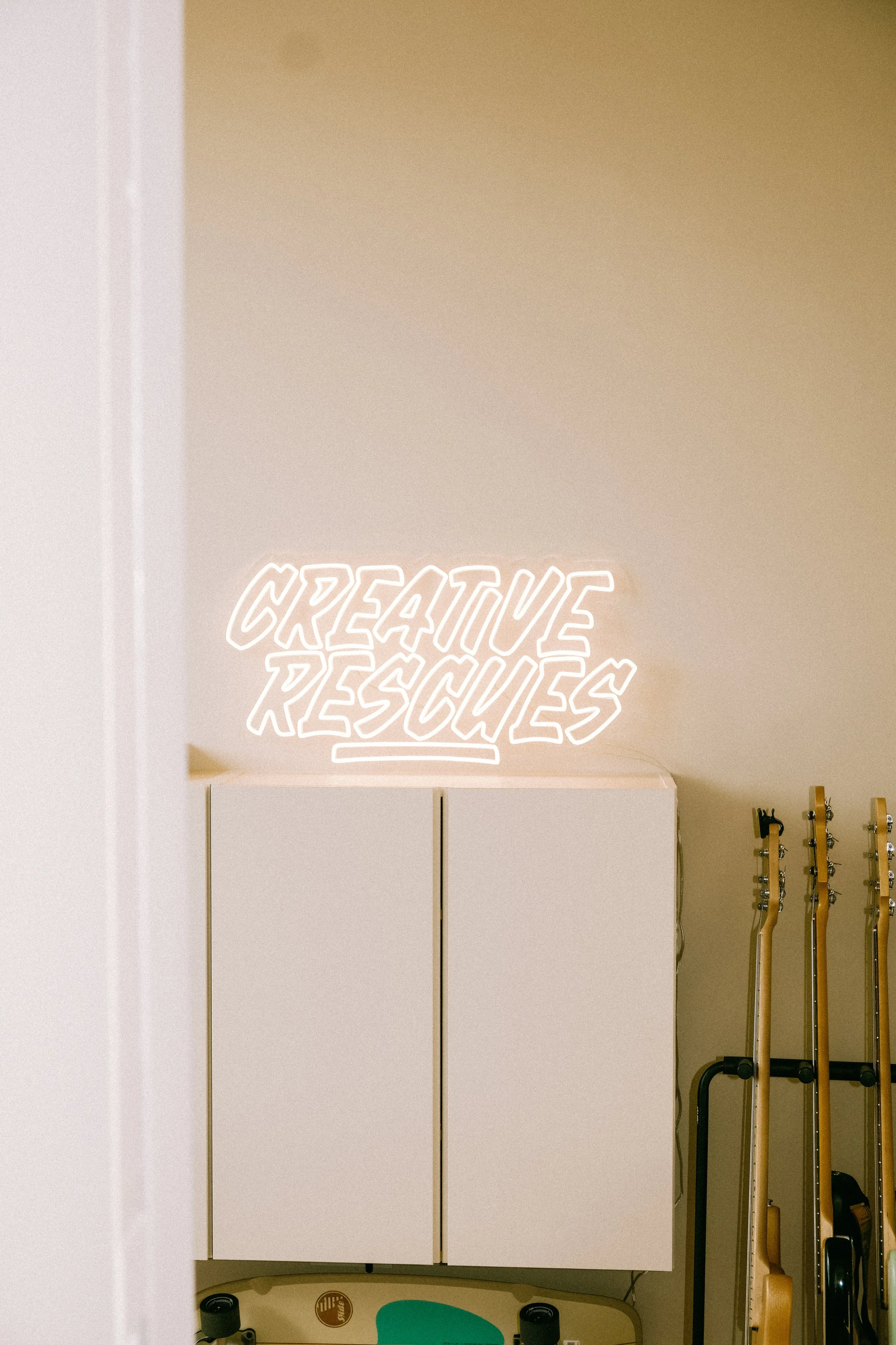 Neonlicht met de woorden 'Creative Rescue' hangt boven witte kasten in een kamer.