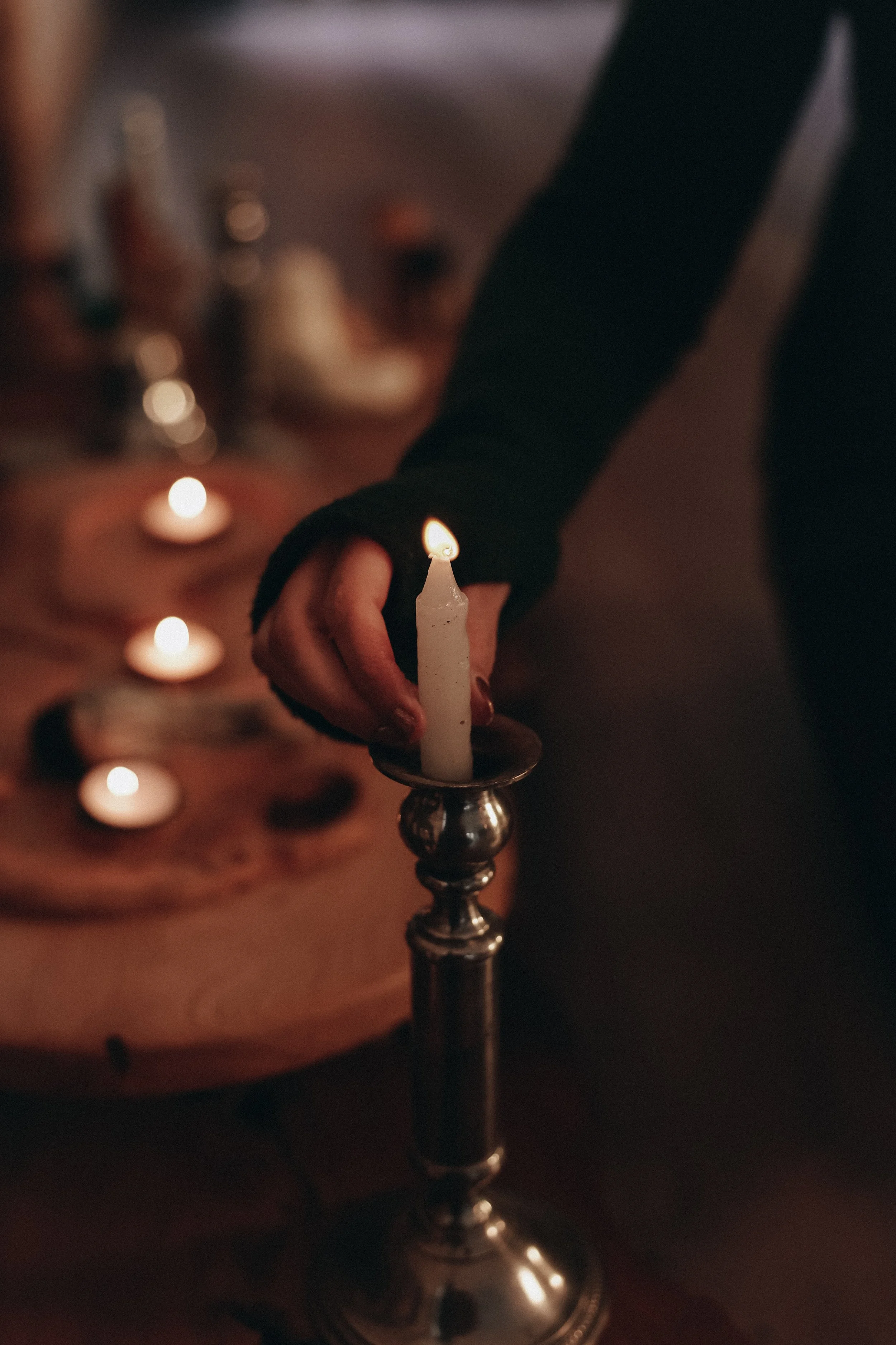 A person’s hand holding a lit candle on a candlestick, with a blurred background of a decorated cake with candles.