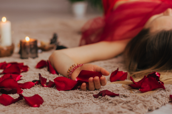 A woman lying on a plush rug surrounded by scattered red rose petals and lit candles.