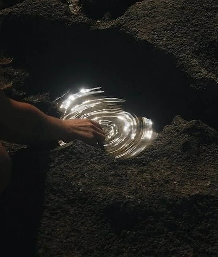 Person touching reflective water inside a rocky cave or crevice with ripples and shining light reflections.