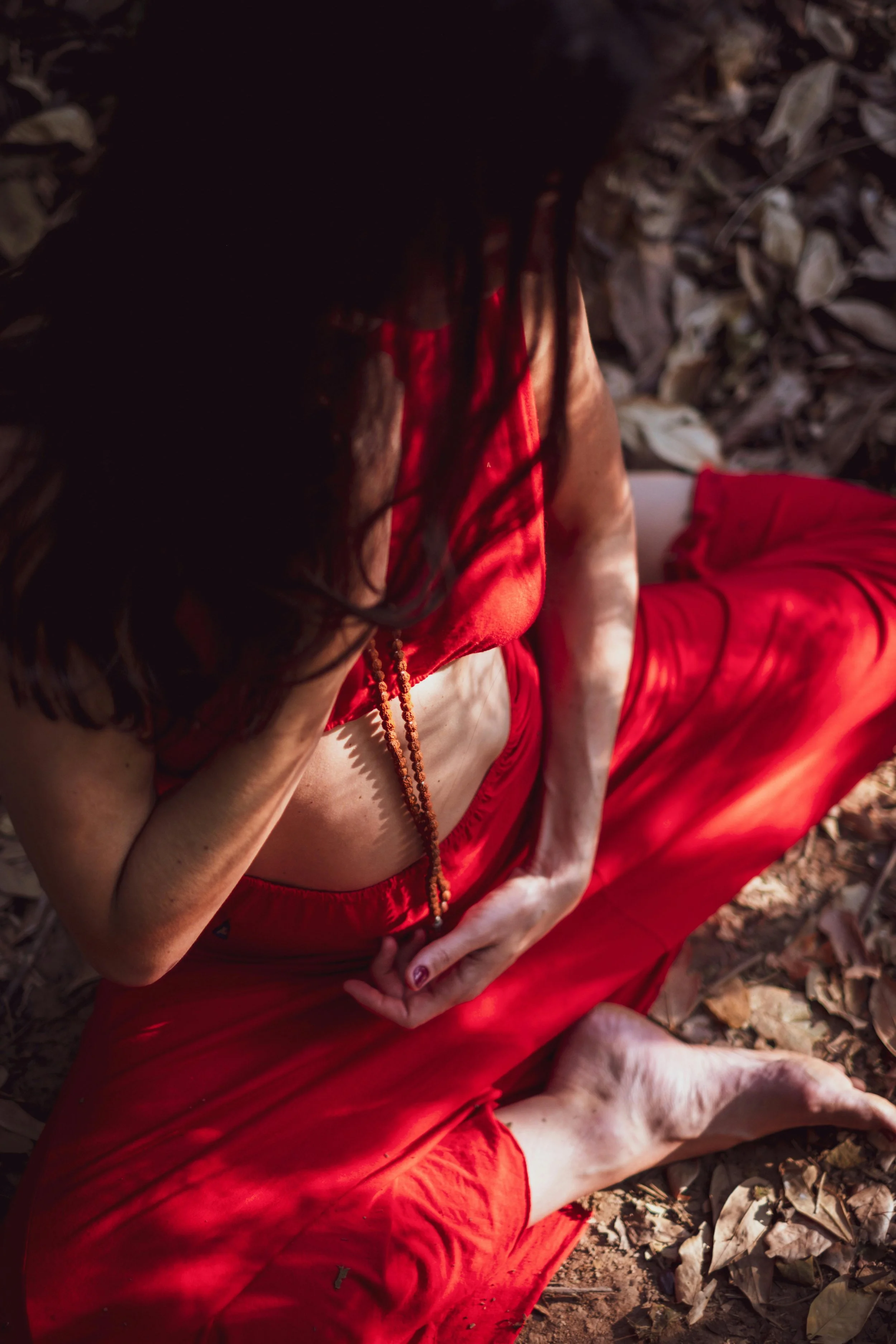 A person lying on the ground surrounded by dry leaves, wearing a red dress, with their hand covering part of their face.