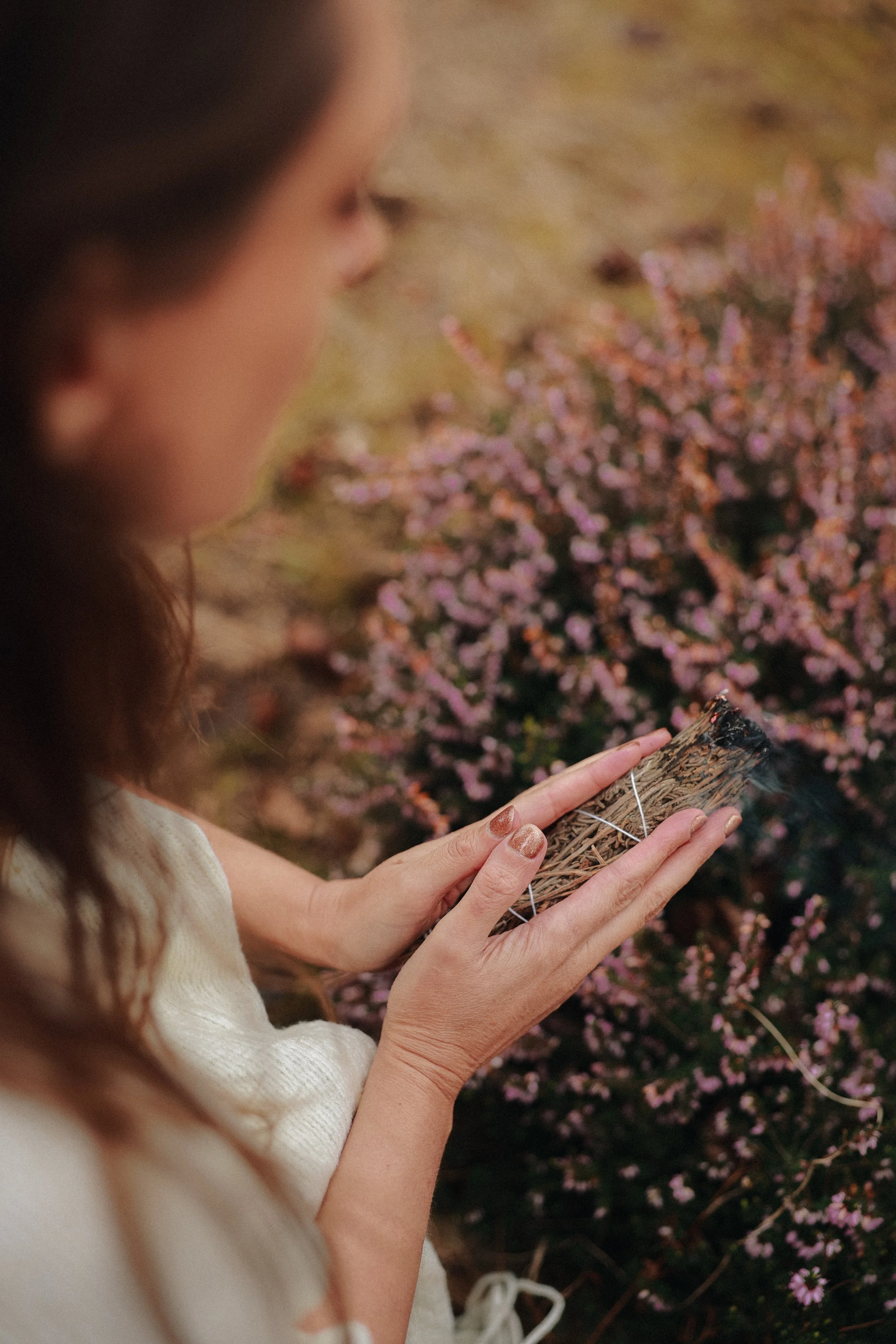 A woman holding a small woven basket outdoors near pink and purple flowers.