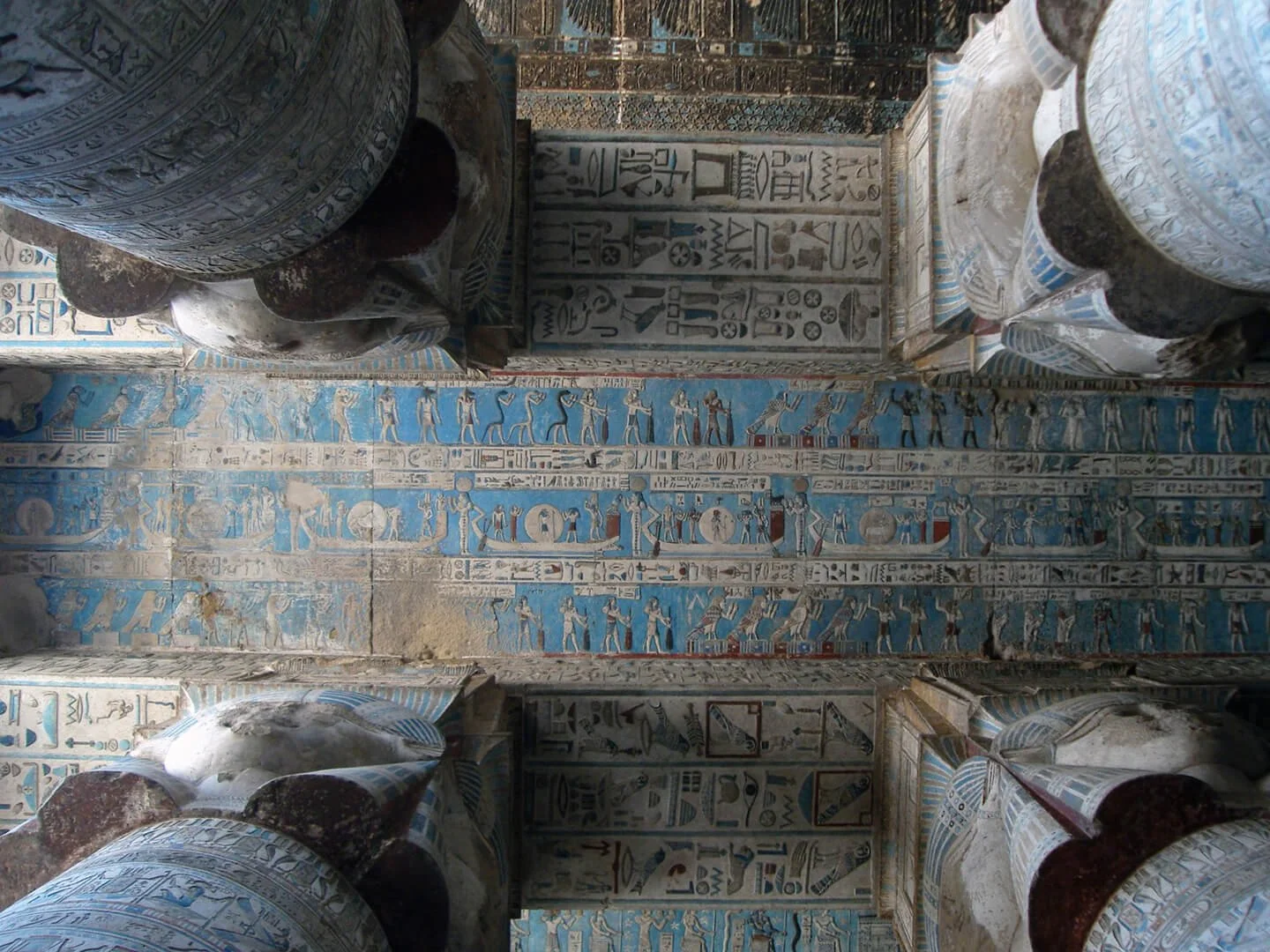 Interior of an ancient Egyptian tomb with painted hieroglyphs and images on the walls and columns.