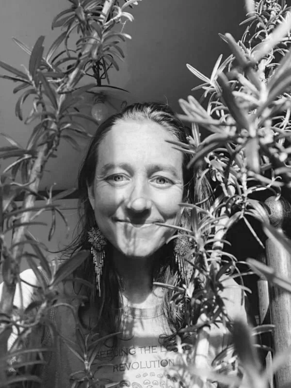 A woman taking a selfie behind a bush with small round fruits, smiling at the camera.