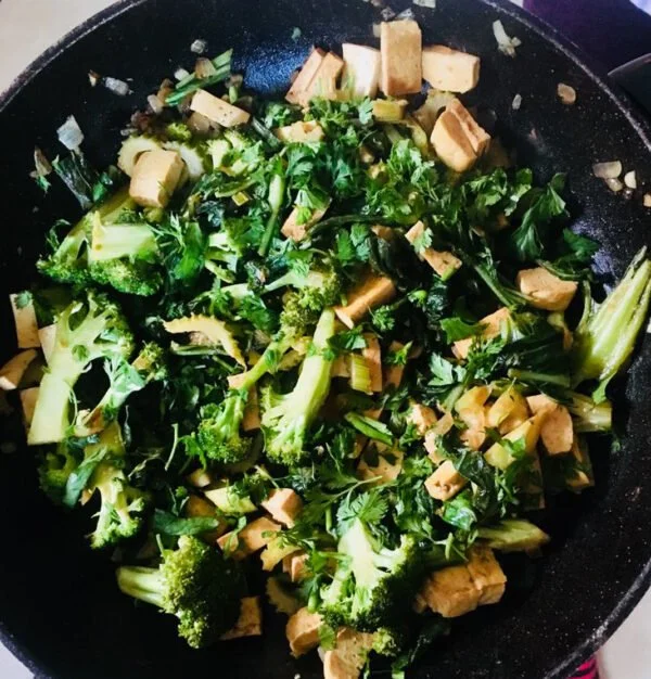 Stir-fried broccoli, kale, onions, and diced tofu in a black skillet.