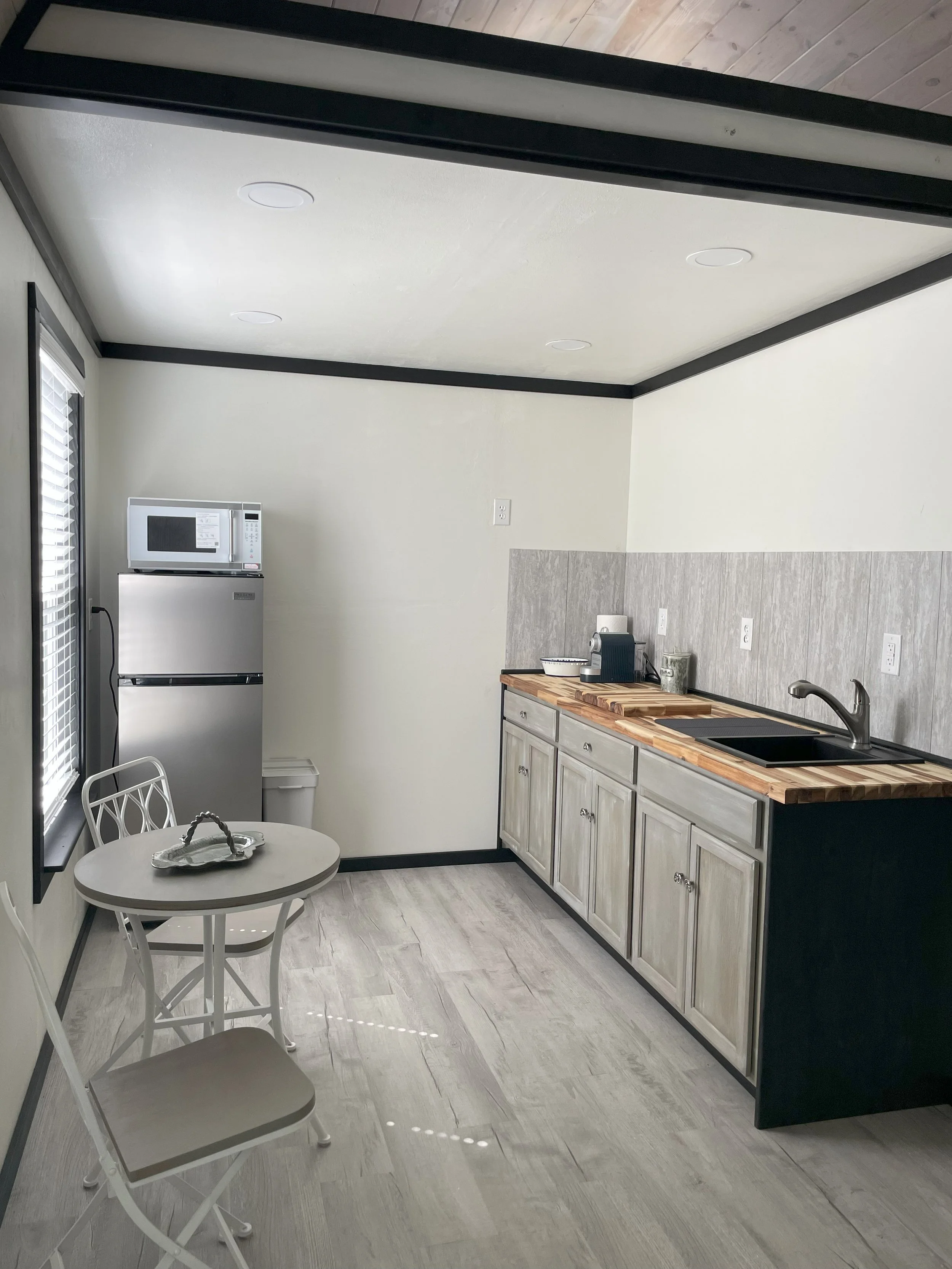 Small kitchen with white walls, black accents, a wooden countertop, a black sink, and a breakfast table with two chairs.