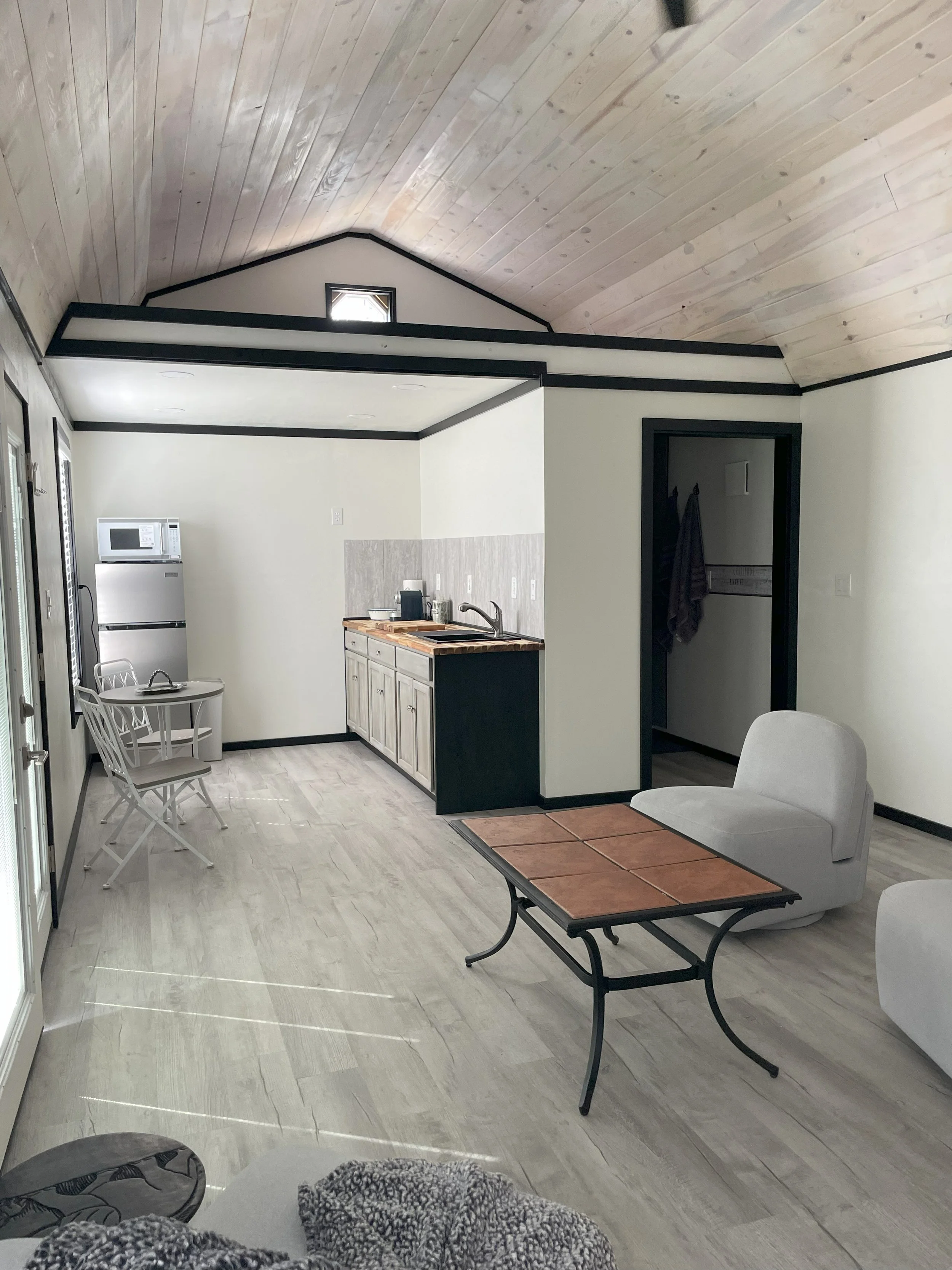 Open-concept living space with a kitchen to the left, dining area with two chairs, and a living area with a white lounge chair and a small table.