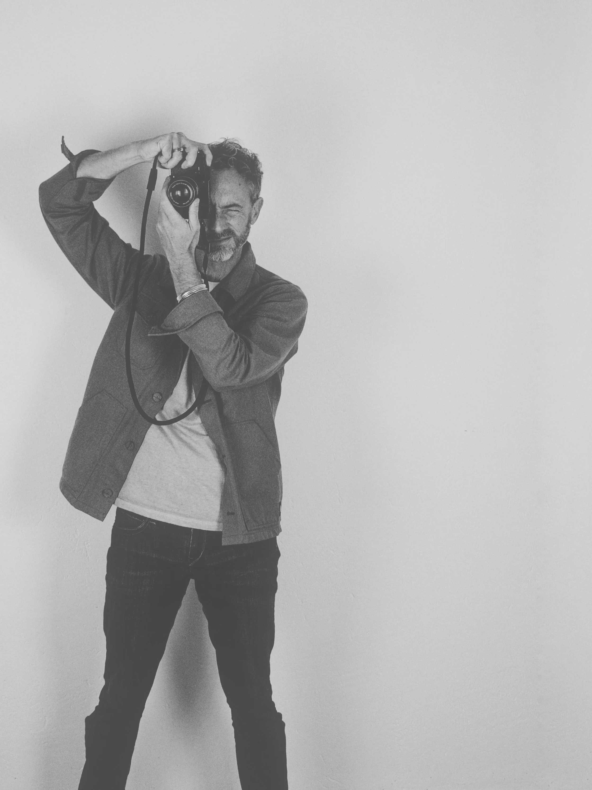 Homme prenant une photo avec un appareil photo reflex, se tenant devant un mur blanc, en noir et blanc