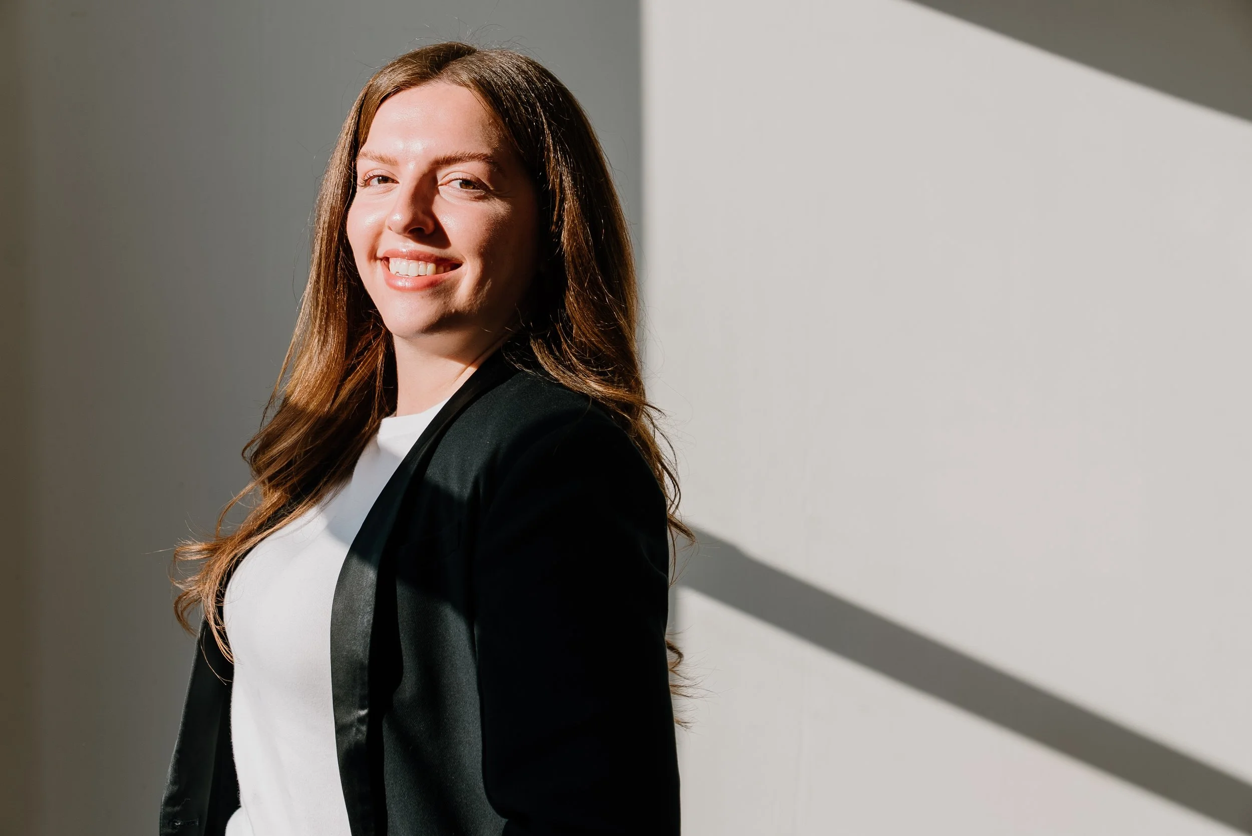Smiling businesswoman in a black blazer standing in warm sunlight