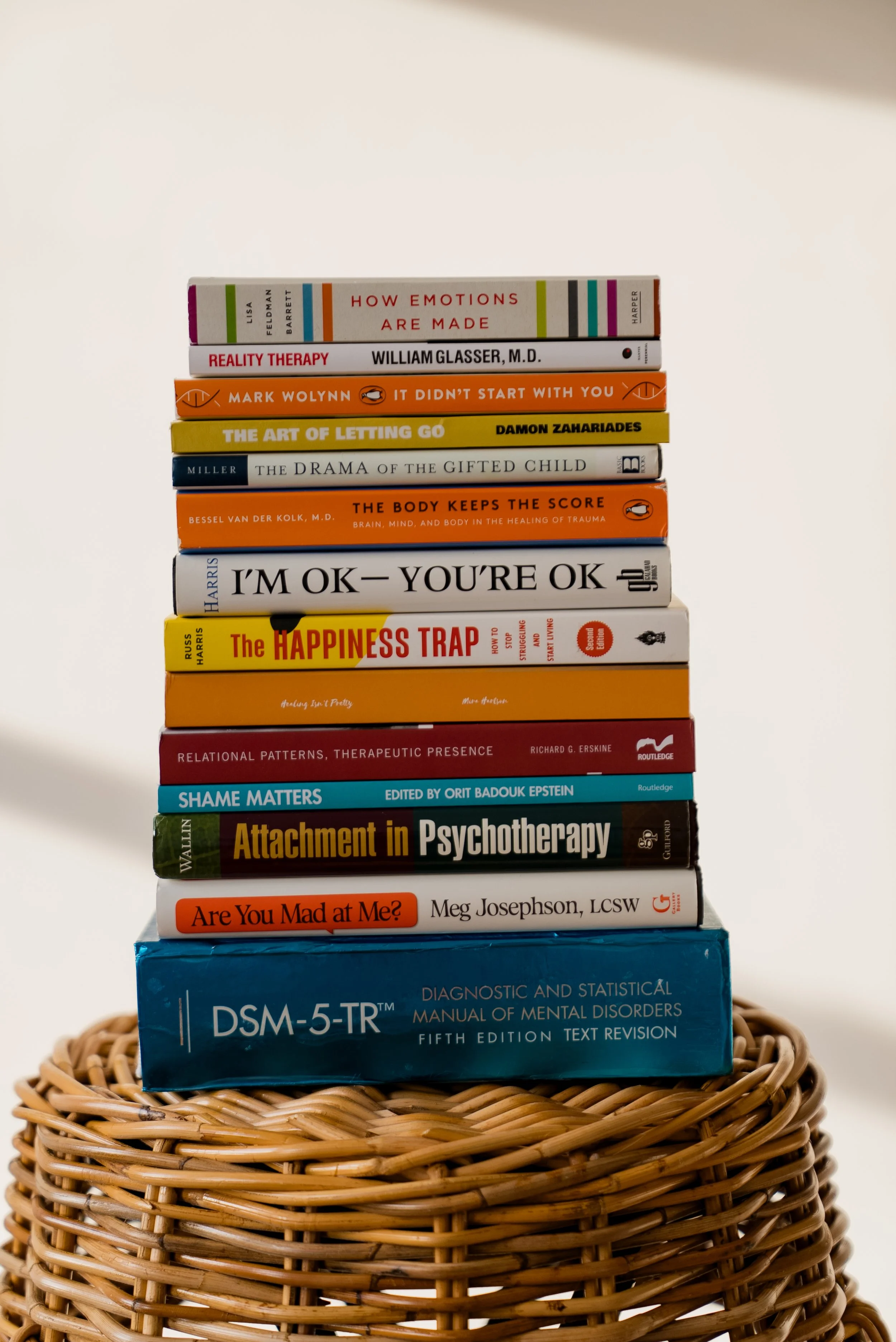 Stack of psychology and self-help books, including the DSM-5-TR, arranged on a woven wicker basket.