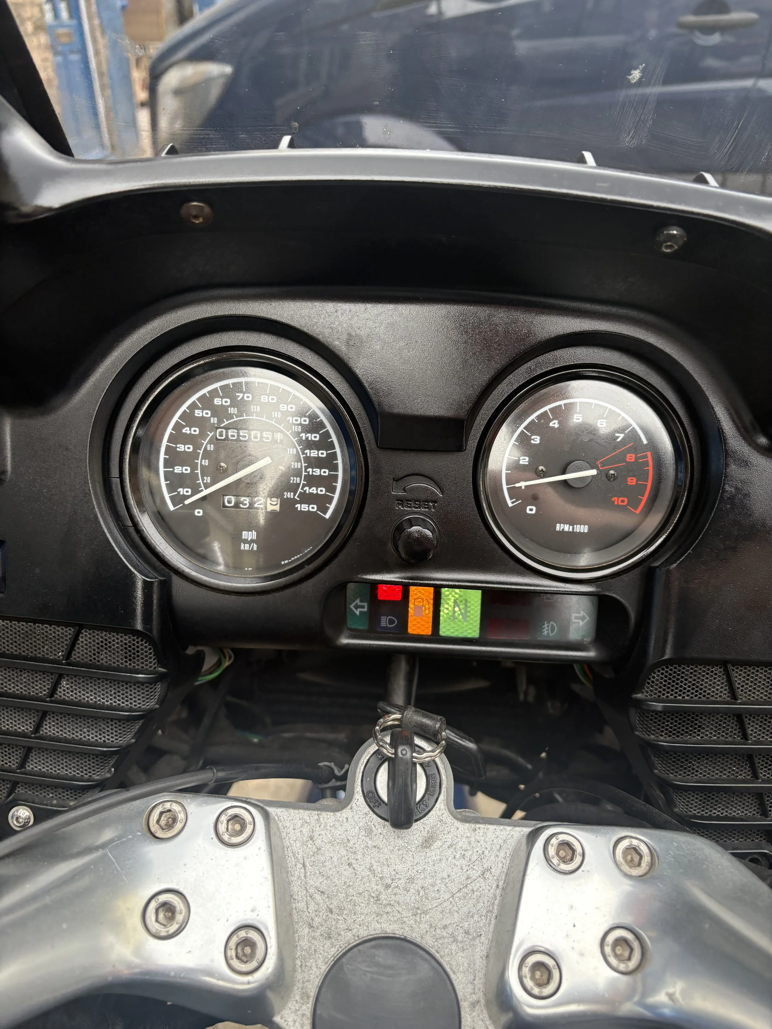 Motorcycle dashboard showing speedometer at 30 mph, tachometer around 1,000 RPM, and indicator lights with green, yellow, and red signals. Key inserted in ignition.