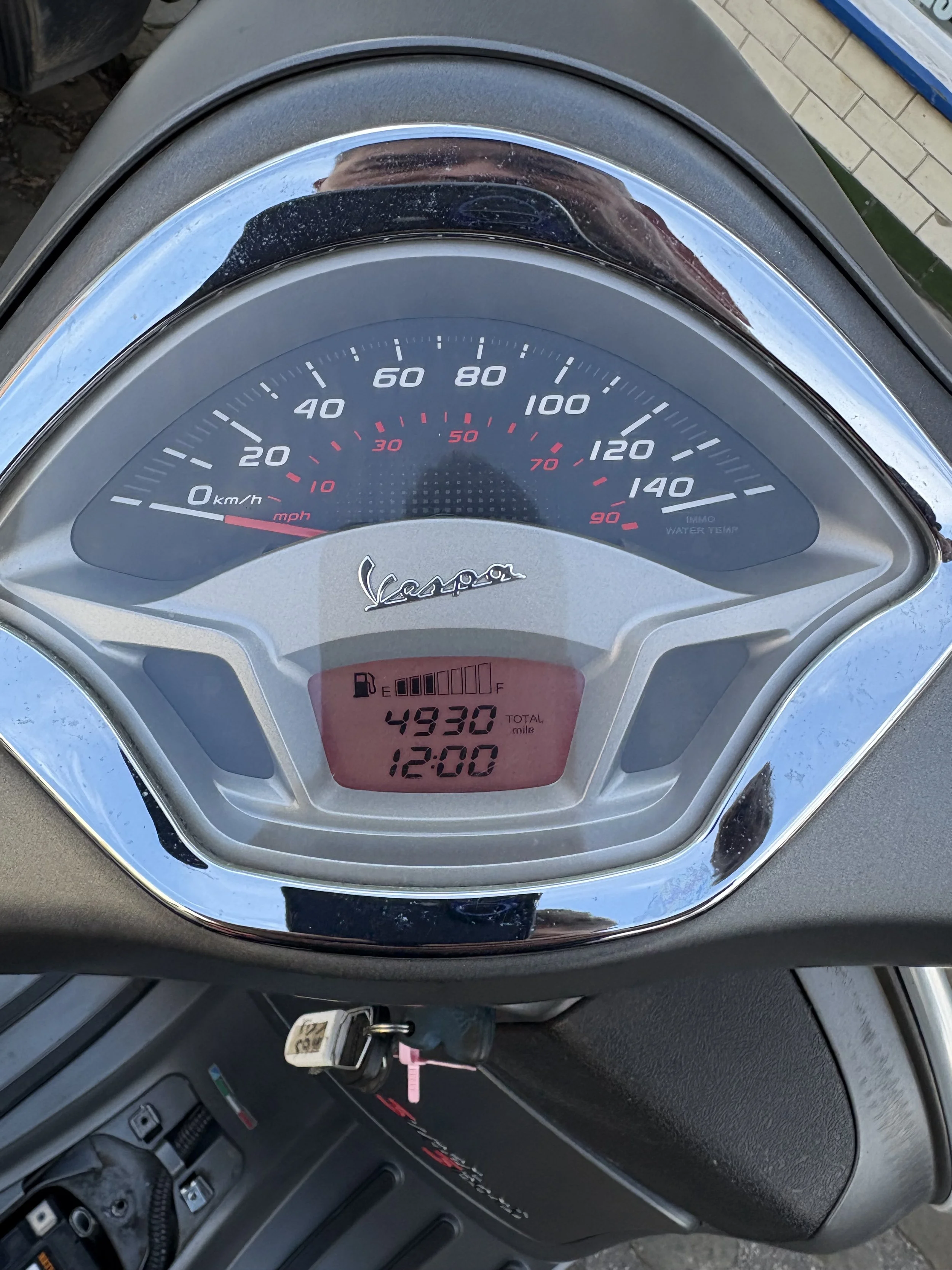 Close-up of a Vespa scooter dashboard including speedometer, fuel gauge, and digital display showing 4930 miles and time 12:00.